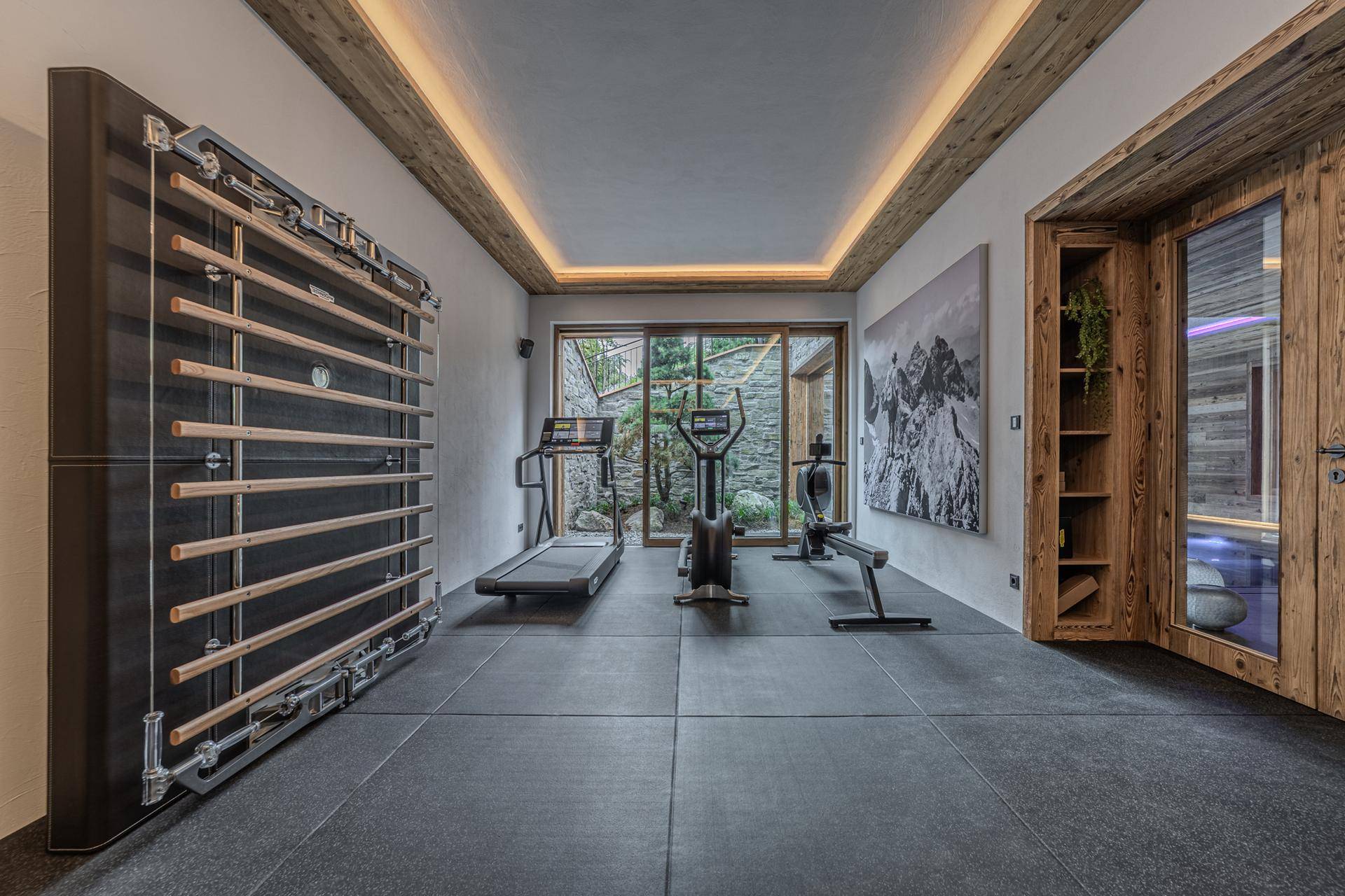 Moderner Fitnessraum mit verschiedenen Trainingsgeräten und Zugang zum Außenbereich.