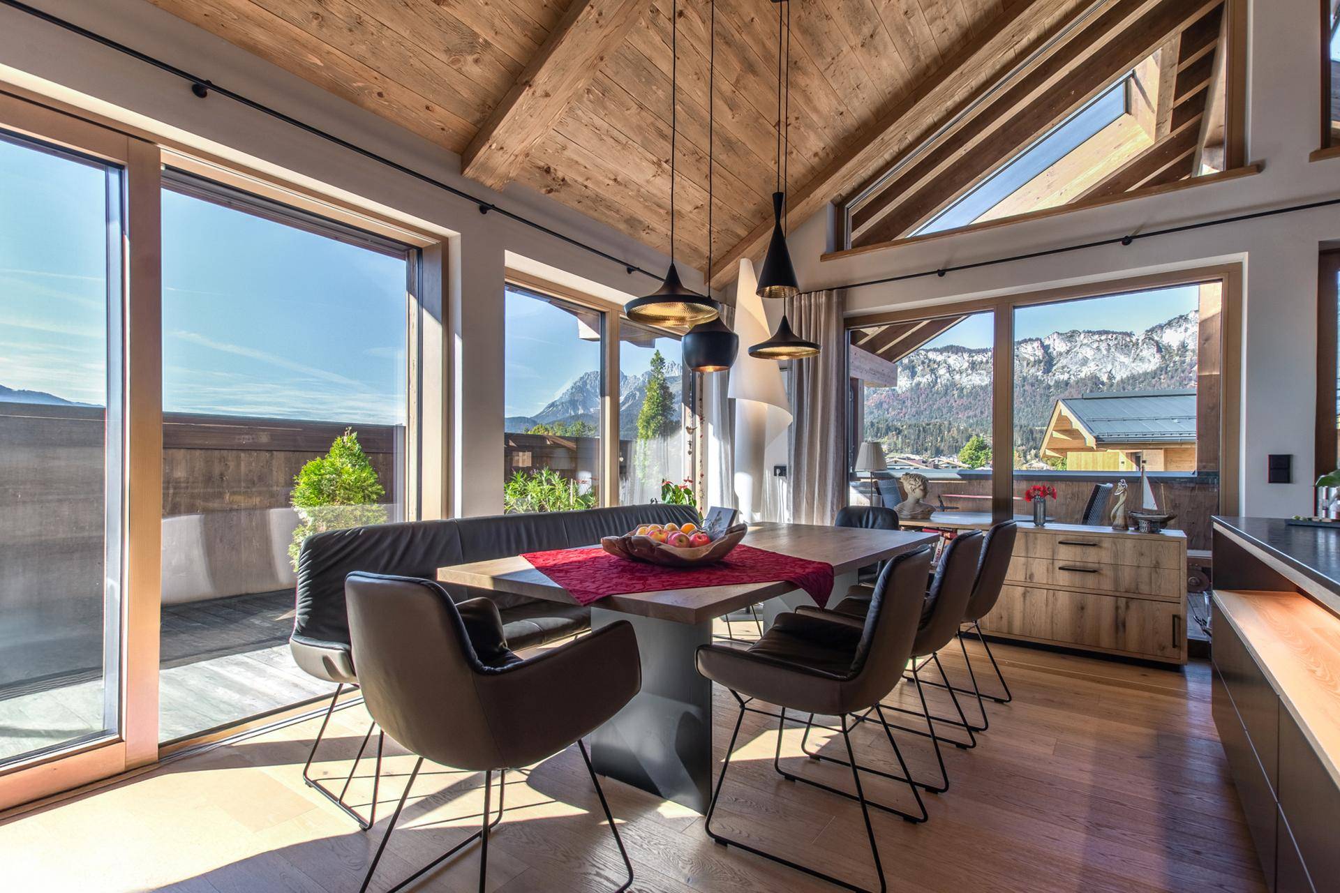 Heller Essbereich mit Holzboden, großen Panoramafenstern und Zugang zur Terrasse mit Bergblick.