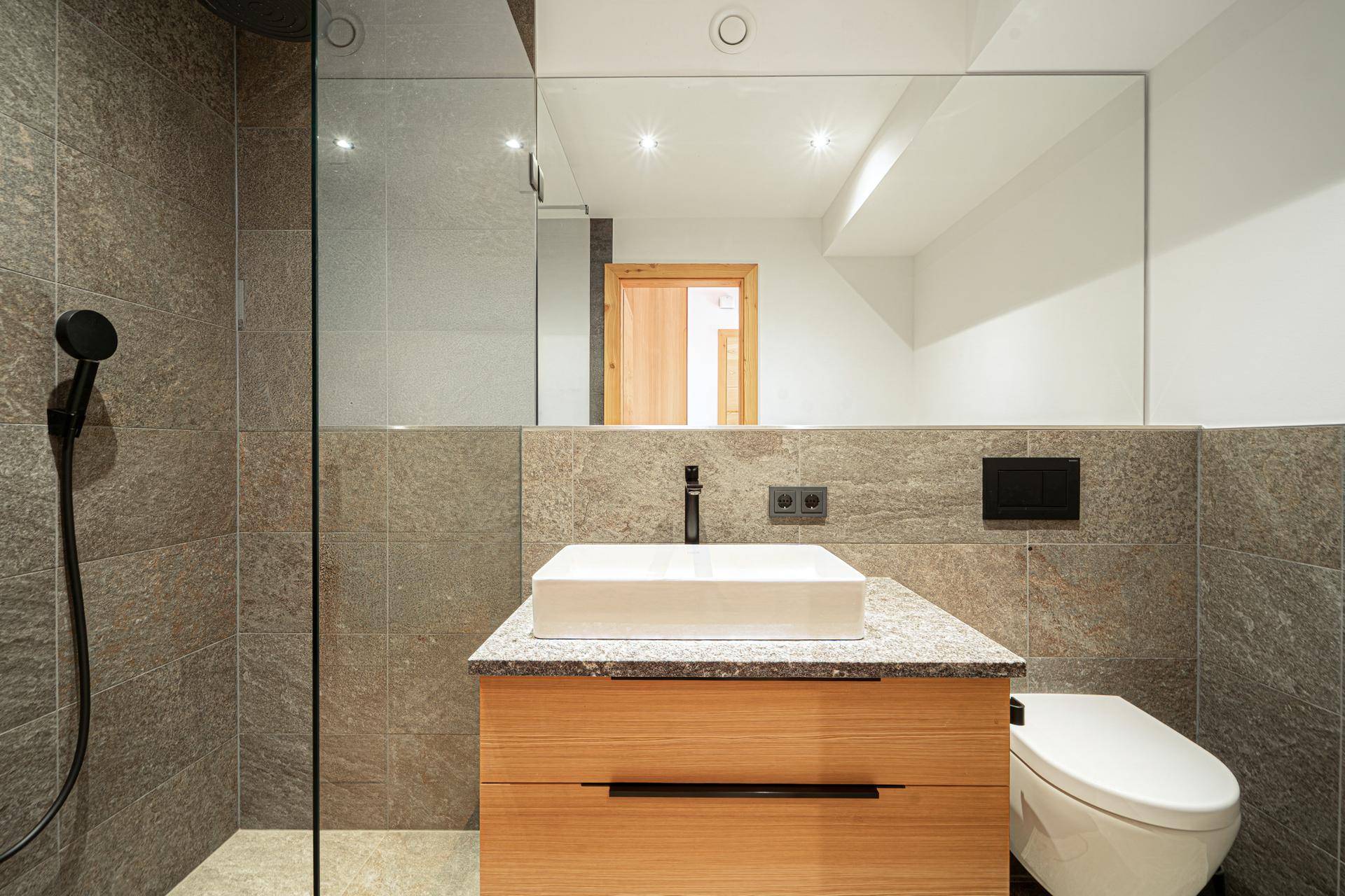 Modernes Badezimmer mit begehbarer Dusche, Waschtisch und Wand-WC in Grautönen.
