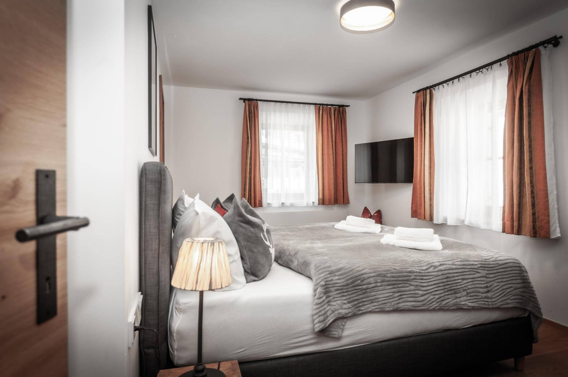 Helles Schlafzimmer mit Doppelbett, Holzboden und zwei Fenstern für viel Tageslicht.