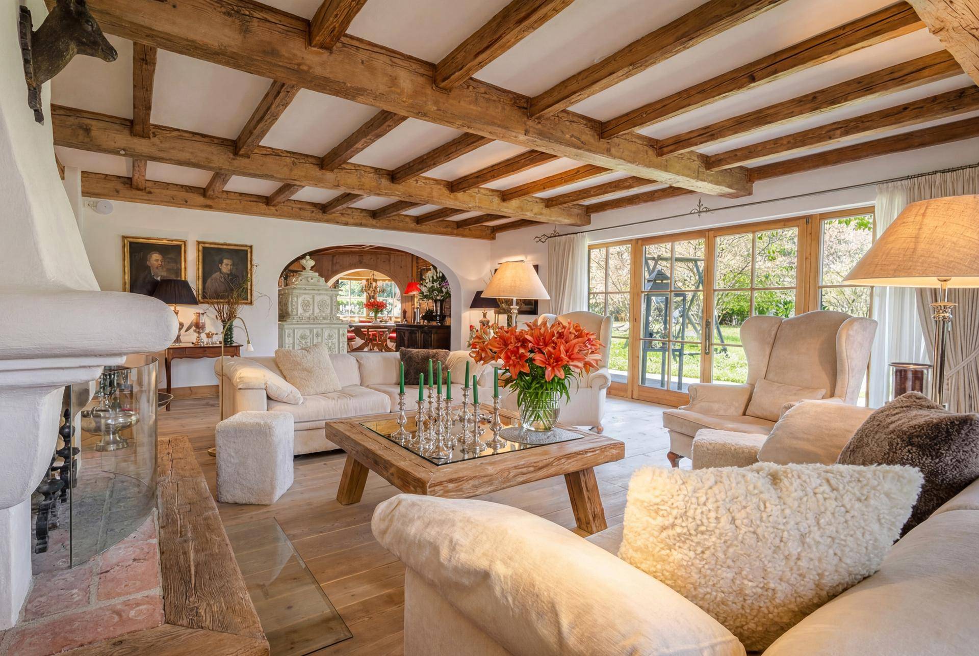 Gemütliches Wohnzimmer mit Holzbalkendecke, Kamin und Zugang zum Garten.