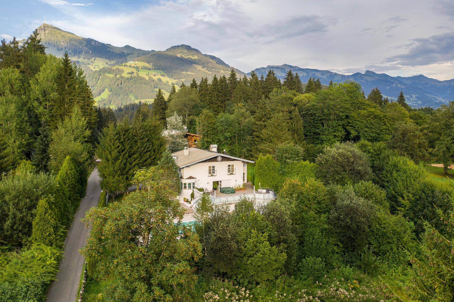 Weitläufige Luftaufnahme des Anwesens, eingebettet in eine grüne Berglandschaft mit vielen Bäumen.
