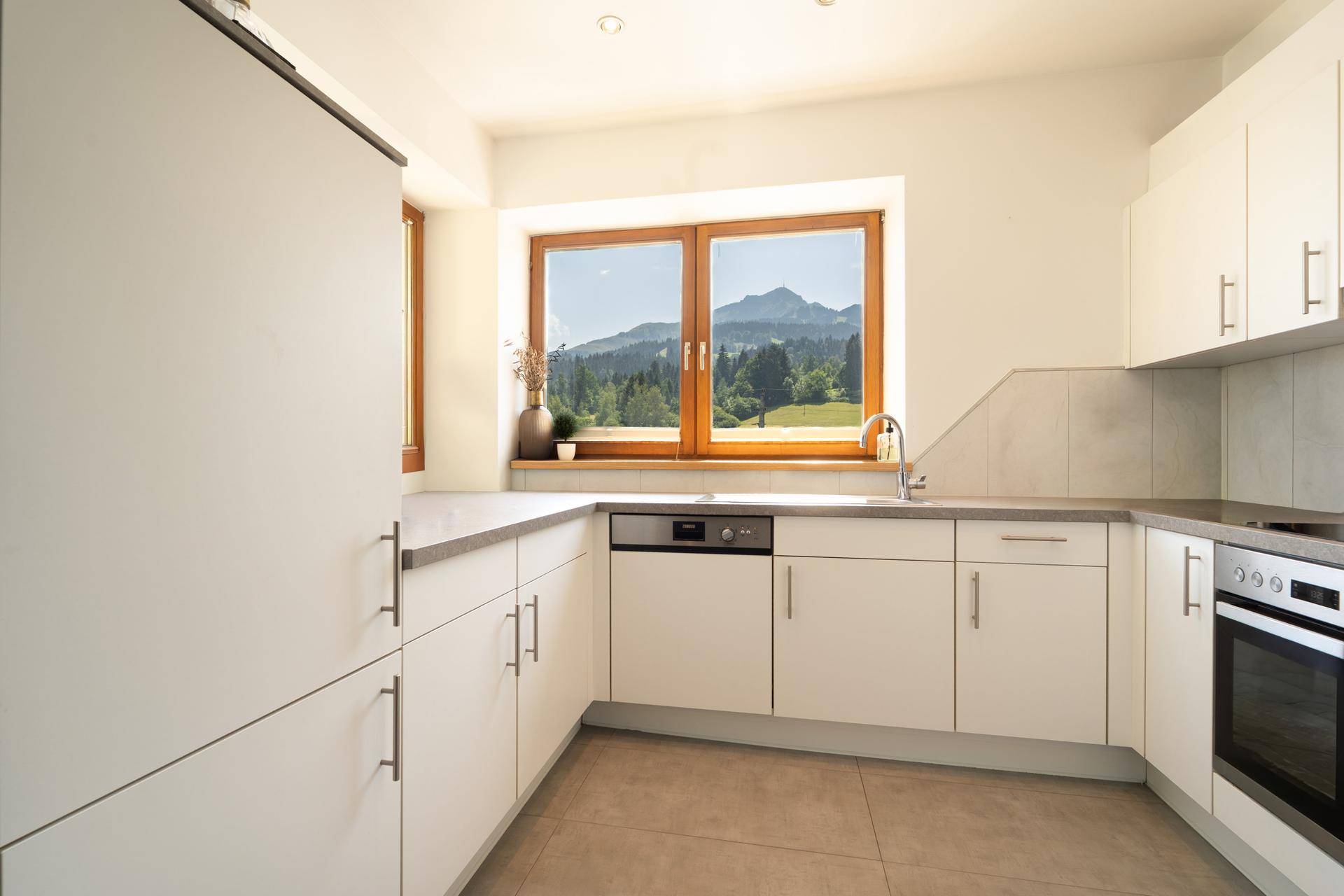 Moderne Einbauküche mit weißen Schränken, Spülmaschine und Bergblick aus dem Fenster.