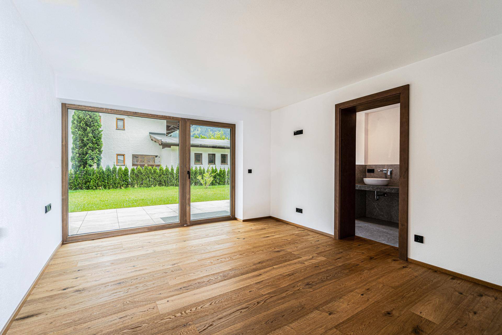Geräumiges Zimmer mit Holzboden, Zugang zum Garten und angrenzendem Badezimmer.