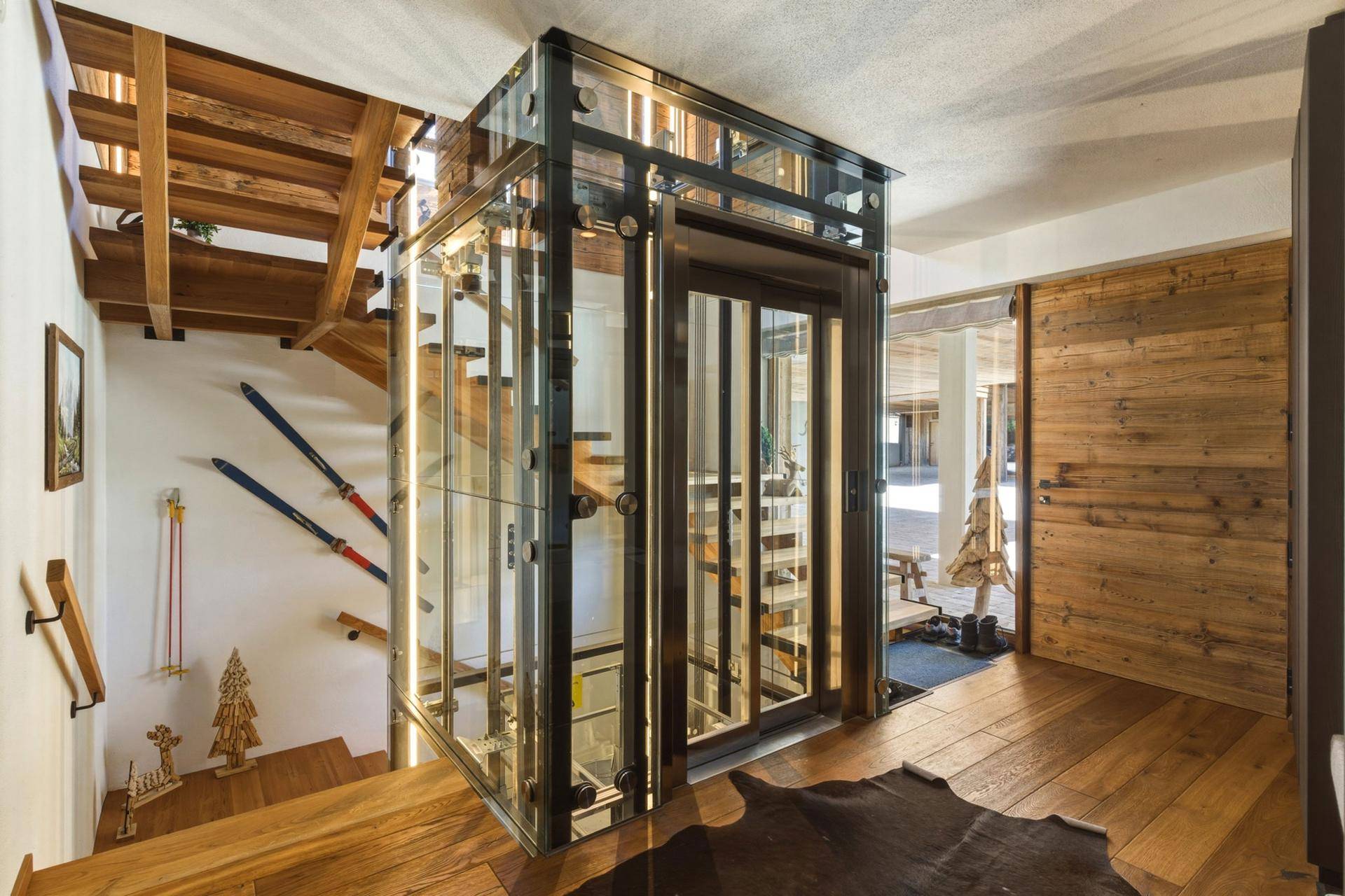 Heller Flur mit moderner Glasliftanlage und Holztreppe.