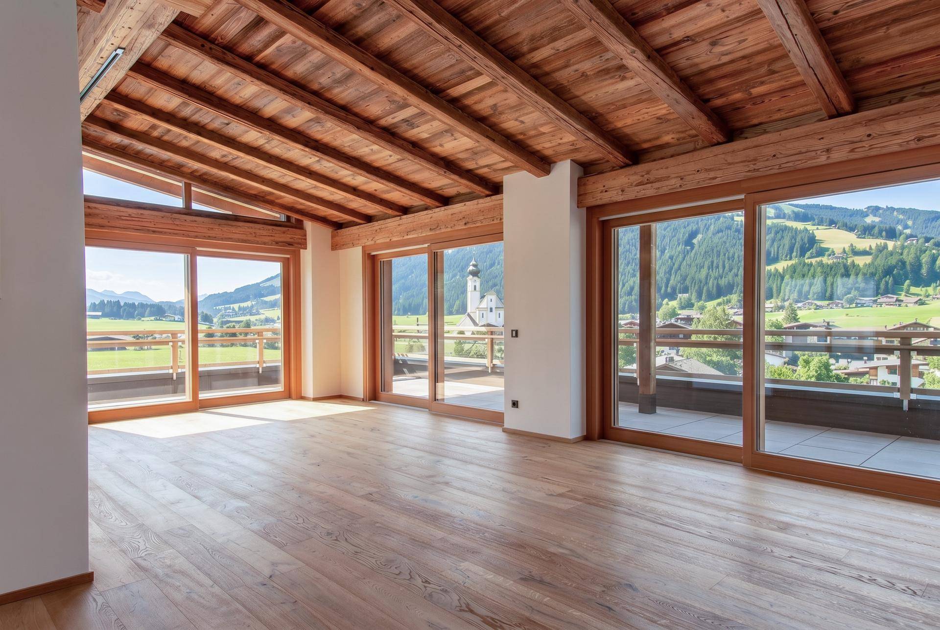Heller Wohnbereich mit Holzboden, Holzbalkendecke und weitem Blick auf die umliegende Landschaft.