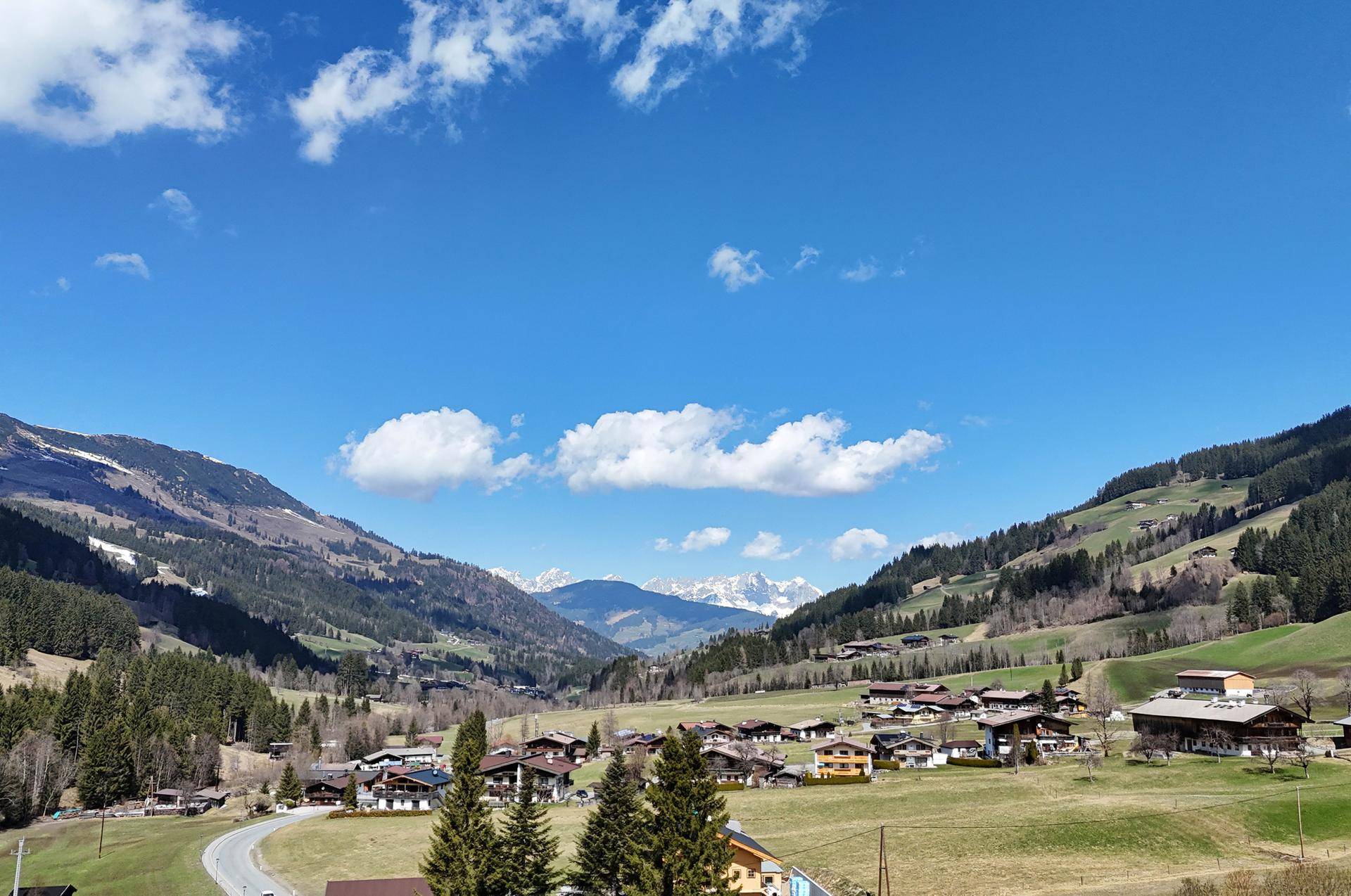 Weitläufiger Blick über ein grünes Tal mit verstreuten Häusern und einer beeindruckenden Bergkulisse im Hintergrund.
