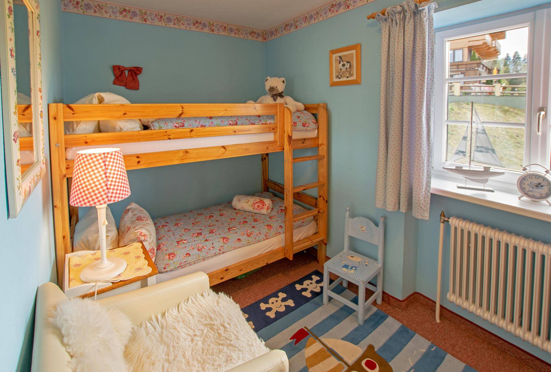 Kinderzimmer mit Etagenbett, blauen Wänden und einem Fenster mit Blick ins Grüne.