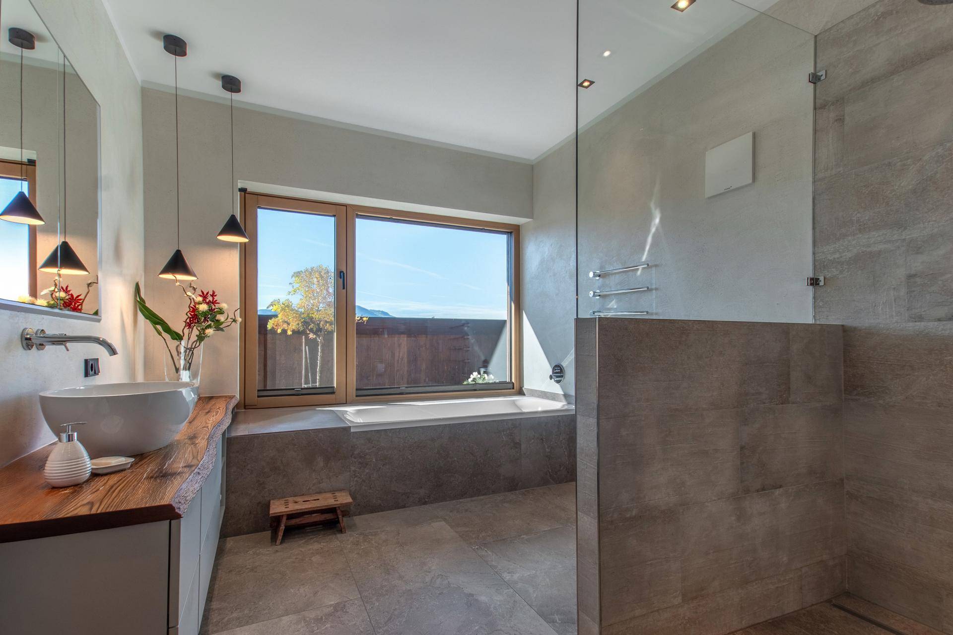 Modernes Badezimmer mit großer Dusche, Badewanne und Fenster mit Blick ins Grüne.
