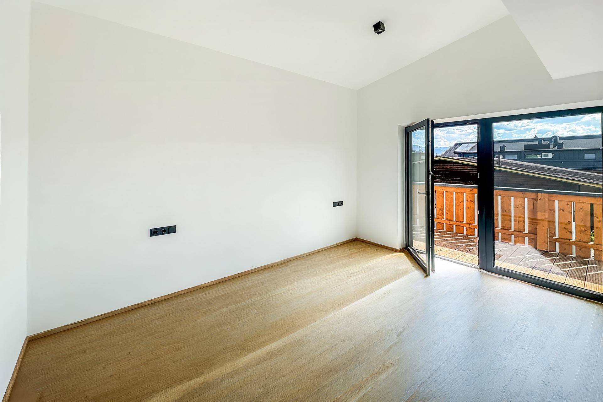 Helles Zimmer mit Holzboden und direktem Zugang zu einem sonnigen Balkon.