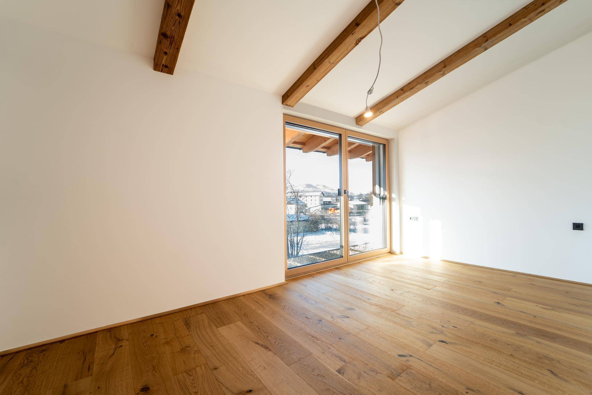 Heller Raum mit Holzboden und großen Fenstern, die viel Tageslicht hereinlassen und einen Ausblick bieten.