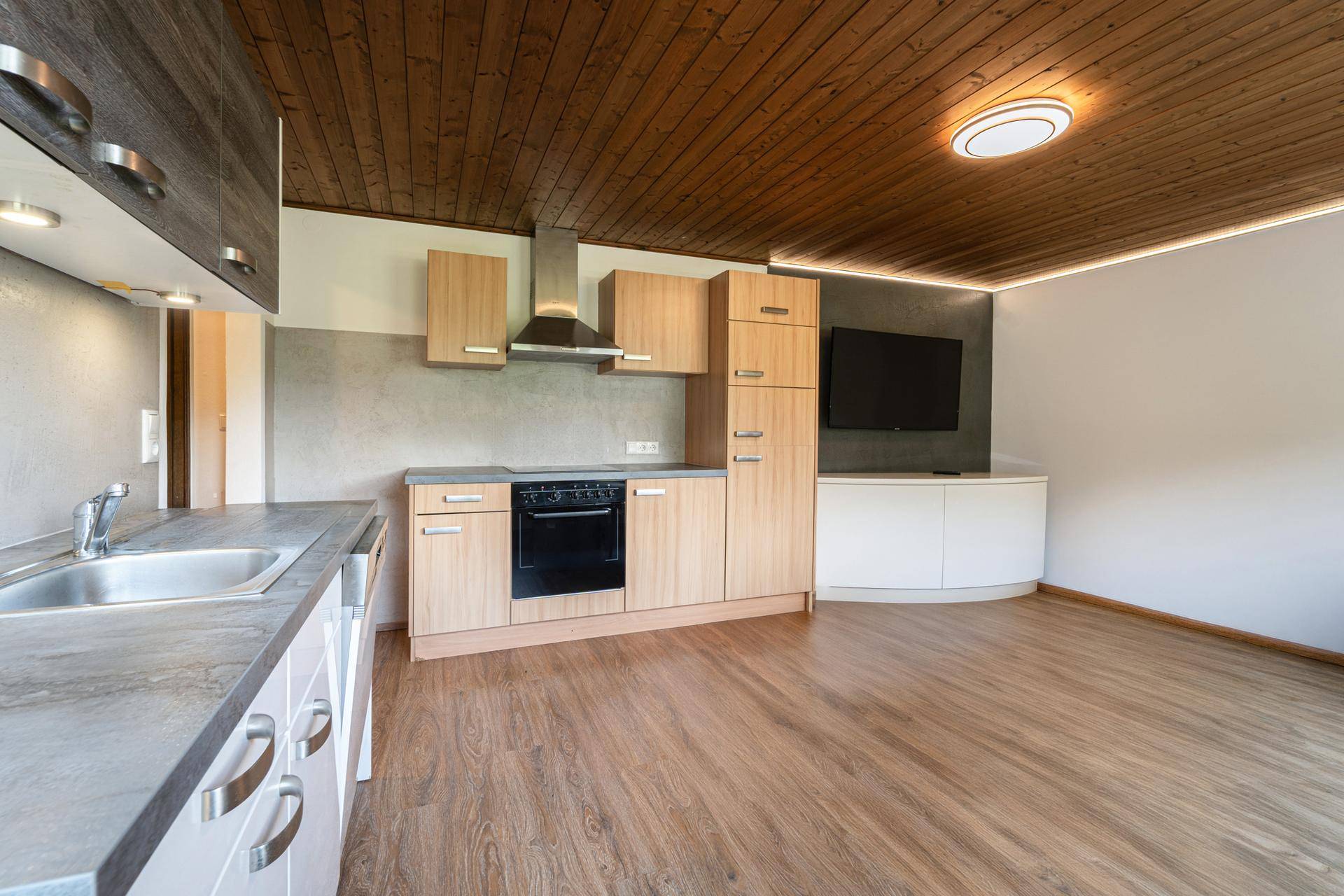 Moderner Küchenbereich mit Holzschränken, integriertem Ofen und angrenzendem Wohnbereich.