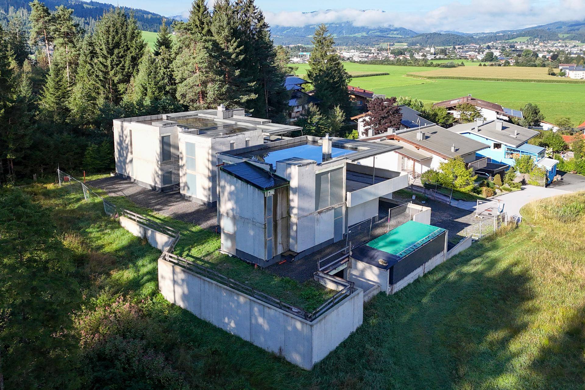 Luftaufnahme des modernen Gebäudes in Betonbauweise, umgeben von Natur und Wald.