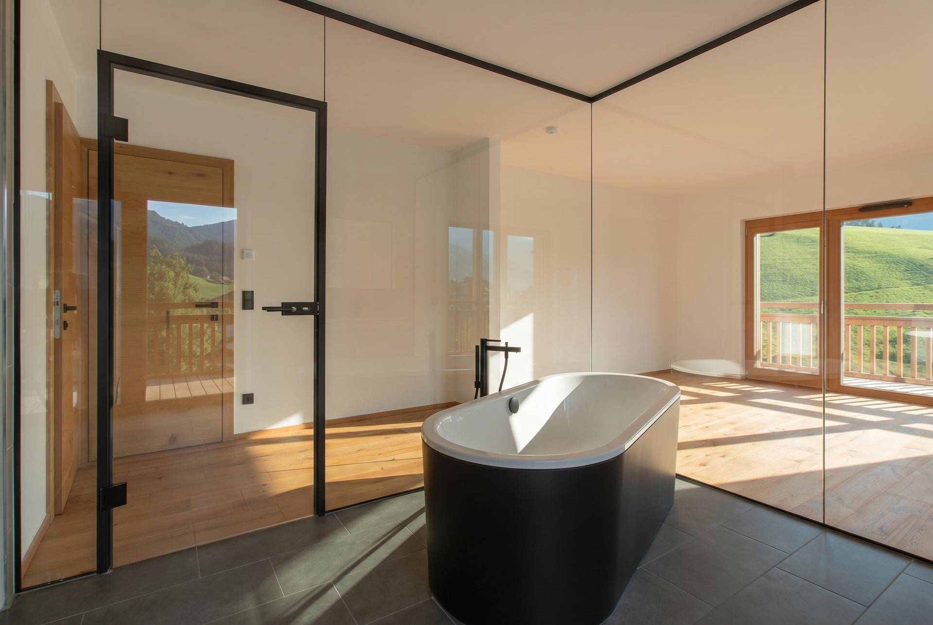 Modernes Badezimmer mit freistehender Badewanne, Glaswänden und Blick auf die Berge.