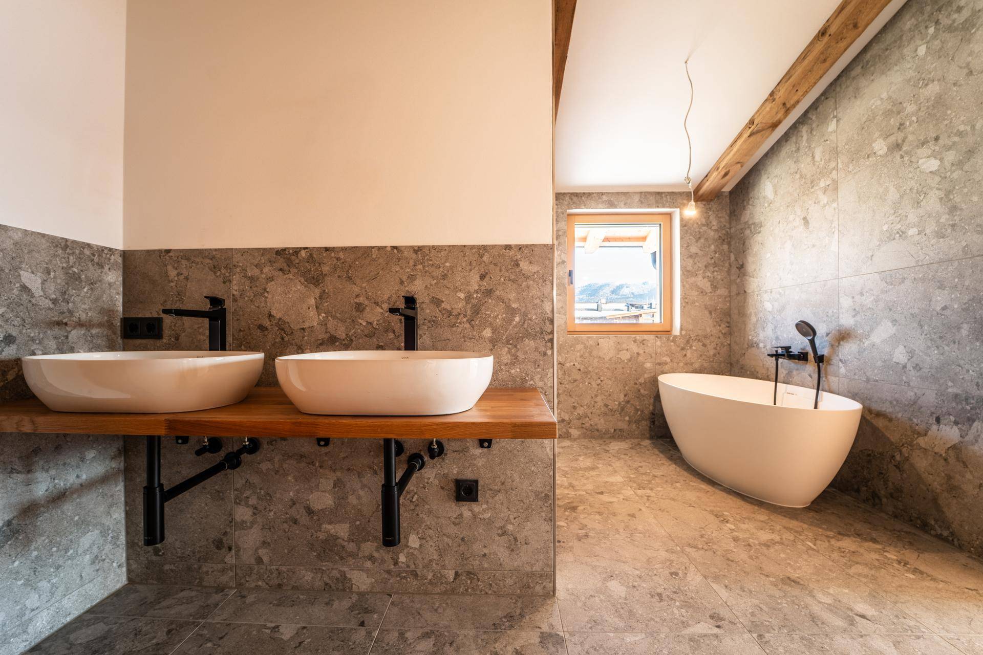 Modernes Badezimmer mit Doppelwaschbecken, freistehender Badewanne und großformatigen Fliesen.