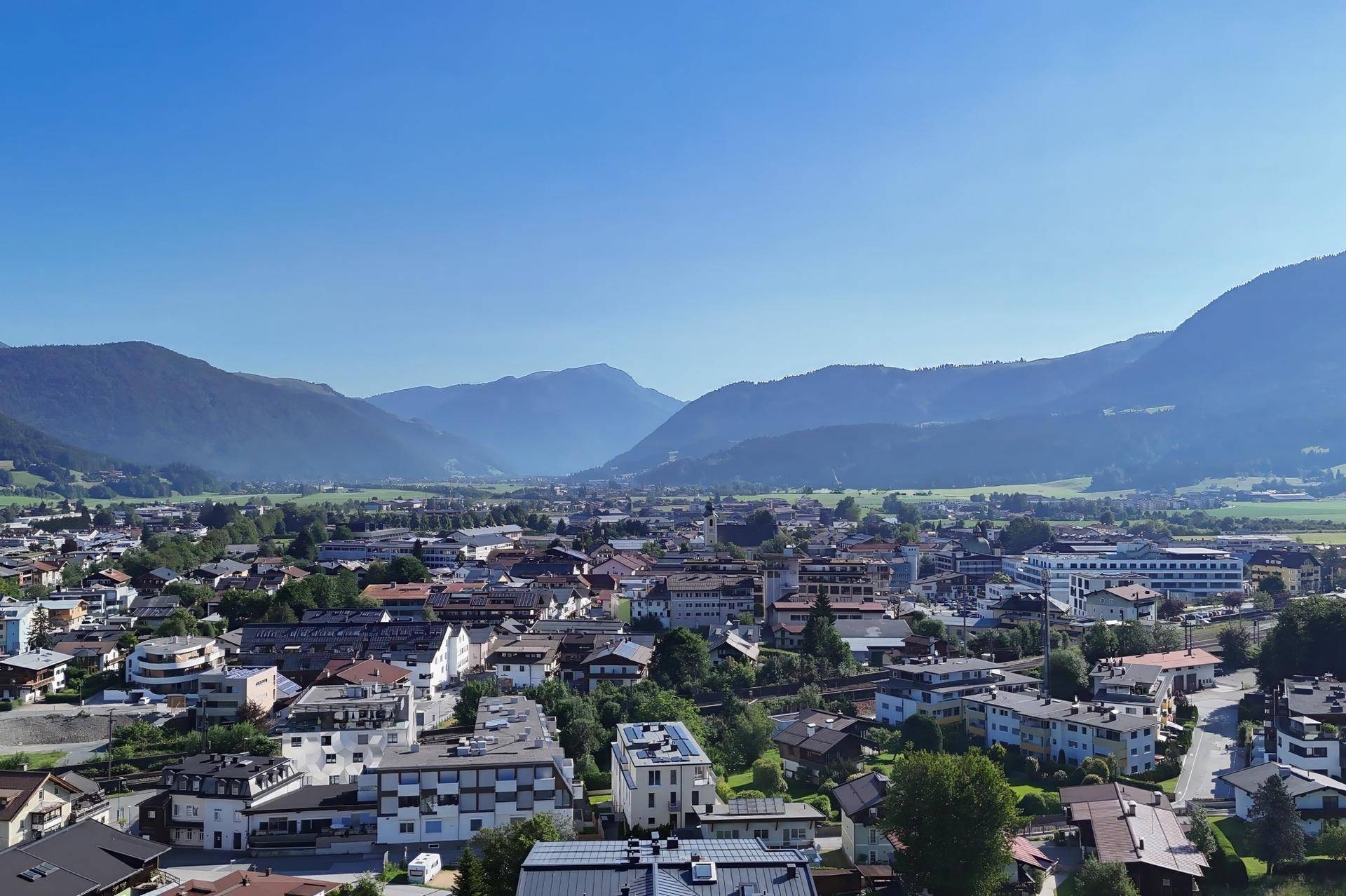 Weitläufige Luftaufnahme einer Stadt in einem Tal, umgeben von grünen Hügeln und Bergen.