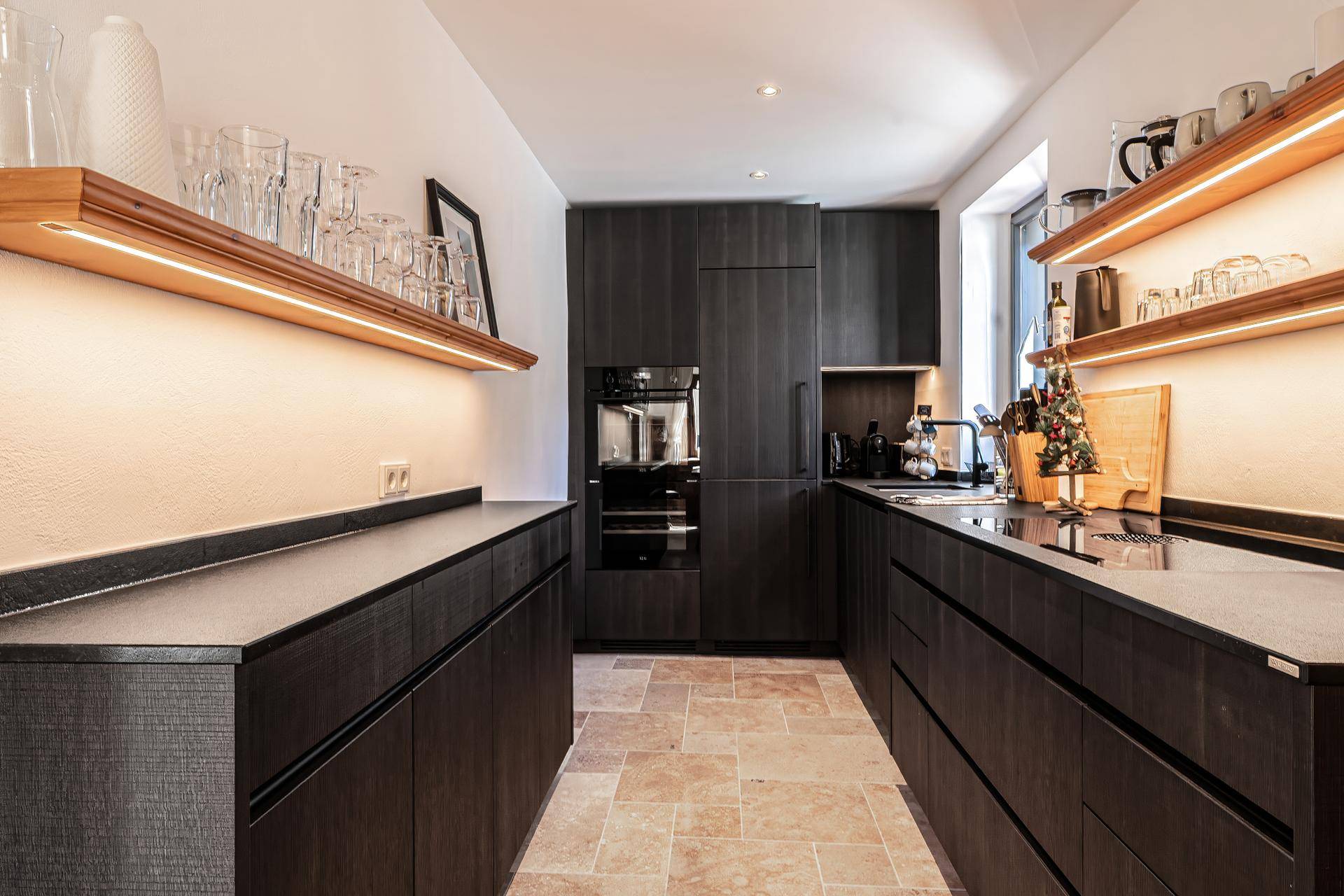 Moderne Küche mit dunklen Holzfronten, integrierten Geräten und beleuchteten Regalen.