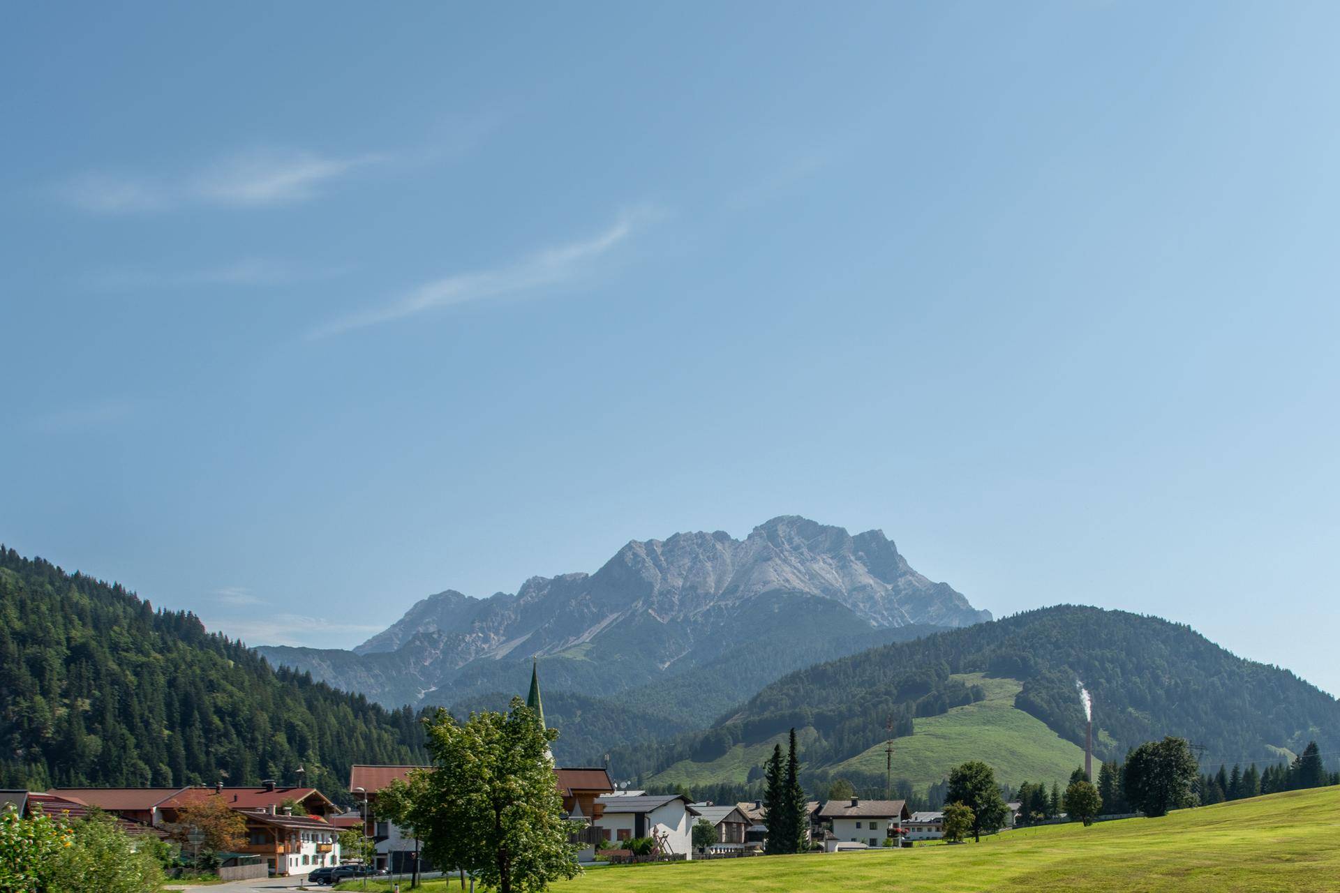 Malerische Berglandschaft mit traditionellen Häusern und üppigem Grün unter einem klaren blauen Himmel.