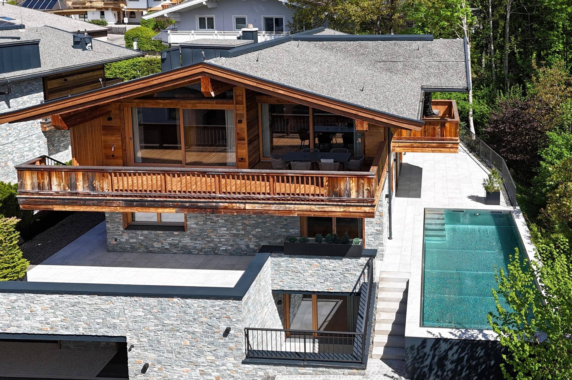Draufsicht auf das moderne Holzchalet mit Außenpool und weitläufigen Terrassenbereichen.