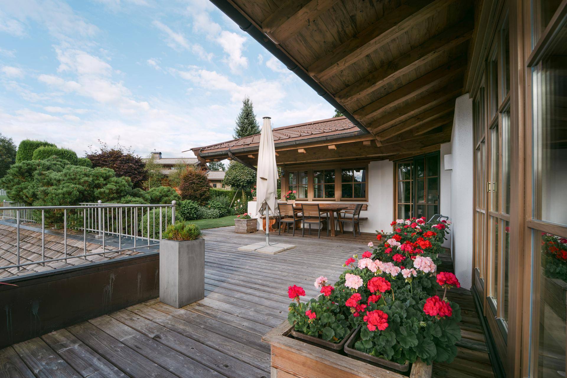 Weitläufige Holzterrasse mit Sonnenschirm und Blumenkästen, bietet viel Platz zum Entspannen im Freien.
