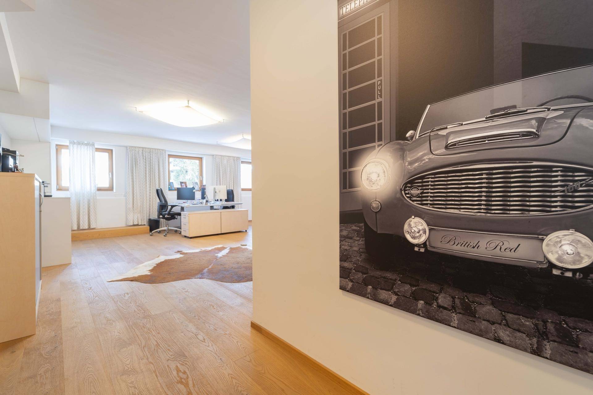 Helles Büro mit mehreren Arbeitsplätzen, Holzboden und einem großen Kunstwerk an der Wand.