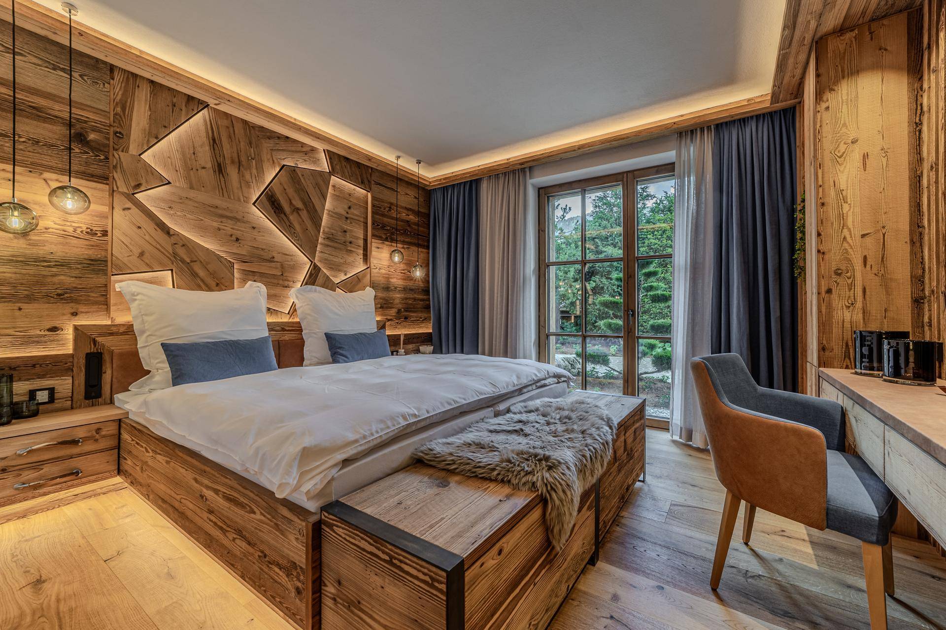 Schlafzimmer mit Holzwandverkleidung, großem Fenster und Blick ins Grüne.