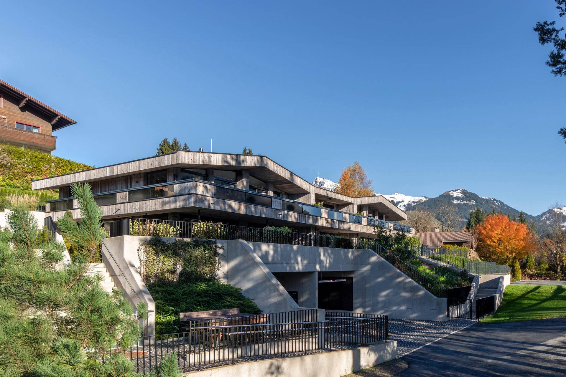 Moderne Architektur des Gebäudes mit mehreren Ebenen, Terrassen und einer beeindruckenden Bergkulisse.