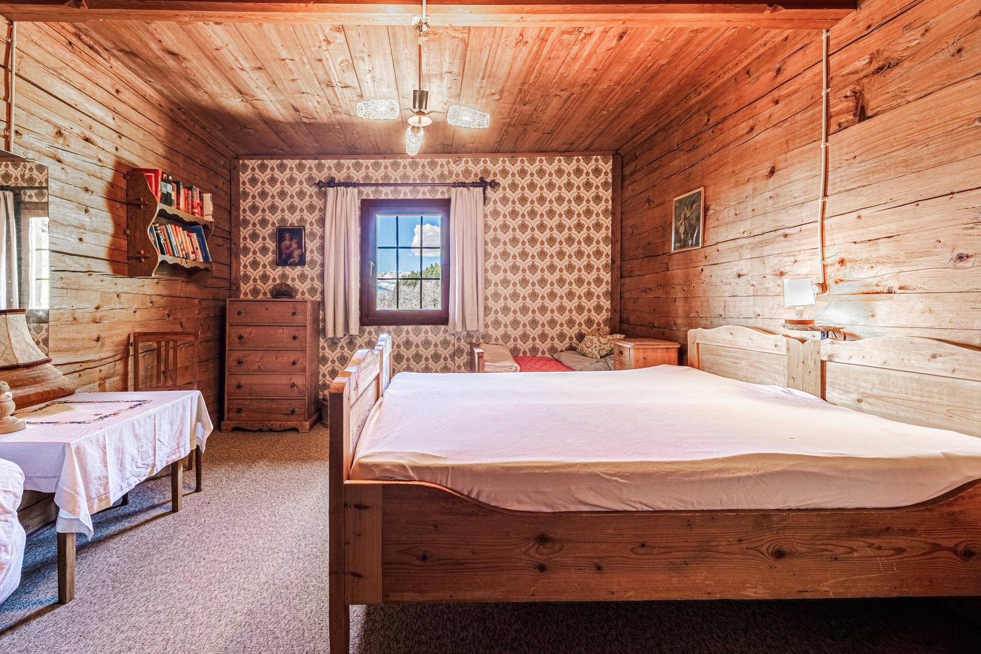 Gemütliches Schlafzimmer mit Holzwänden, Teppichboden, traditionellem Bett und gemusterter Tapete.