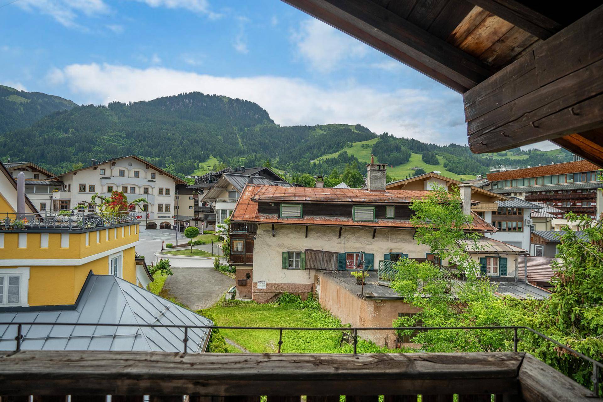 Blick von einem Balkon auf die charmante Alpenstadt und die umliegende Berglandschaft mit traditionellen Gebäuden.