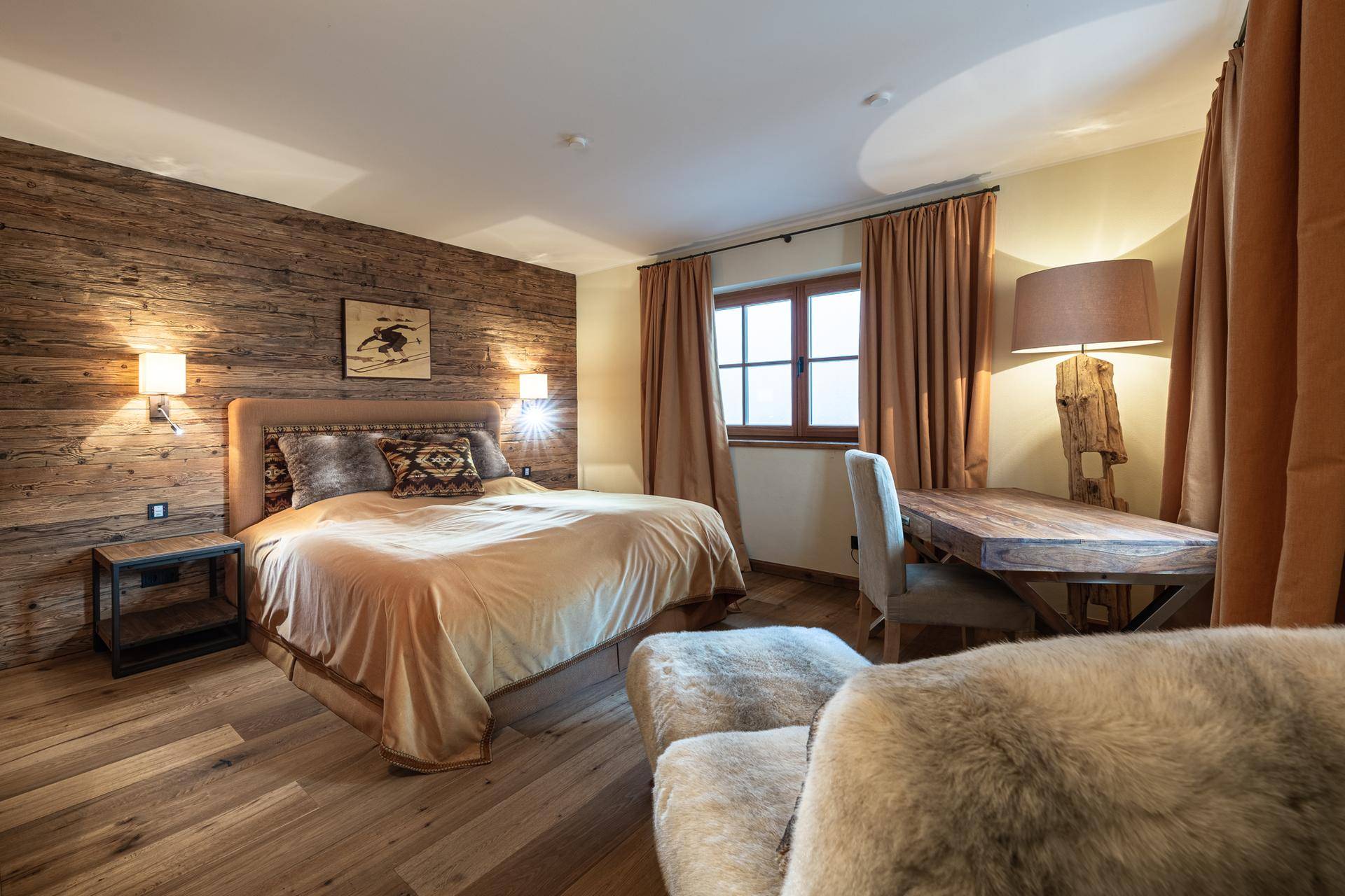 Komfortables Schlafzimmer mit Holzwand, großem Bett und Schreibtisch im alpinen Stil.