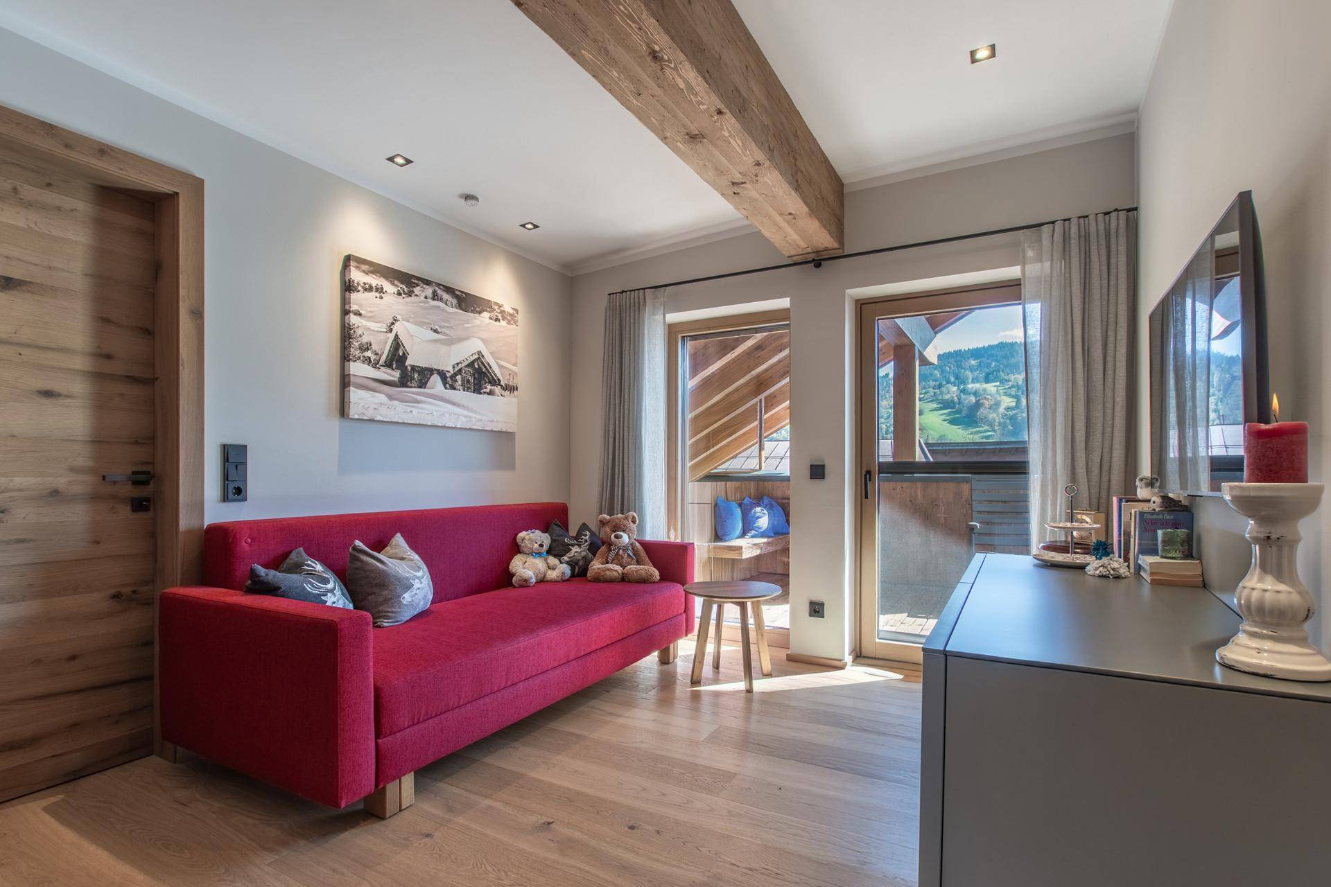Helles Wohnzimmer mit rotem Sofa, Holzbalken und Zugang zu einem kleinen Balkon mit grüner Aussicht.