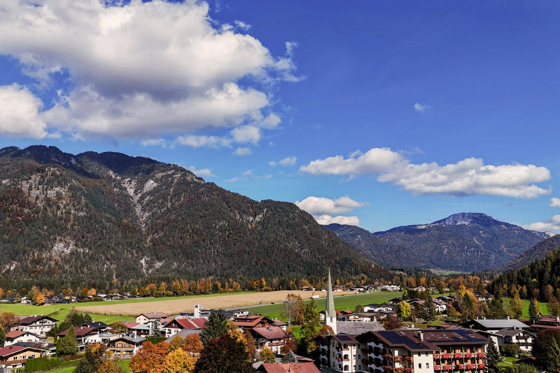 Panoramablick auf eine malerische Berglandschaft mit einem Dorf im Tal unter blauem Himmel.