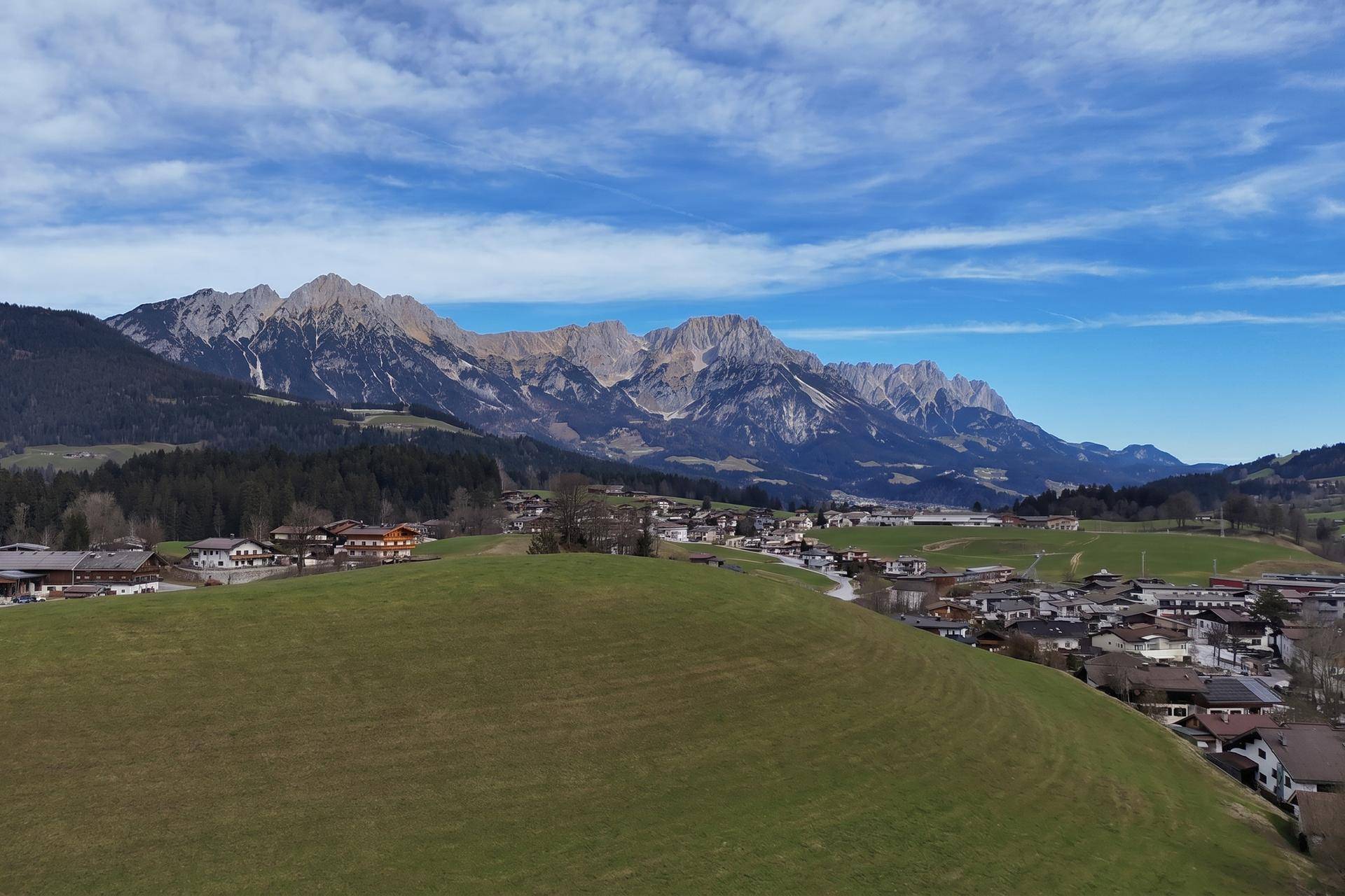 Weitläufige Landschaftsaufnahme mit Bergen, grünen Hügeln und einer Siedlung im Tal.