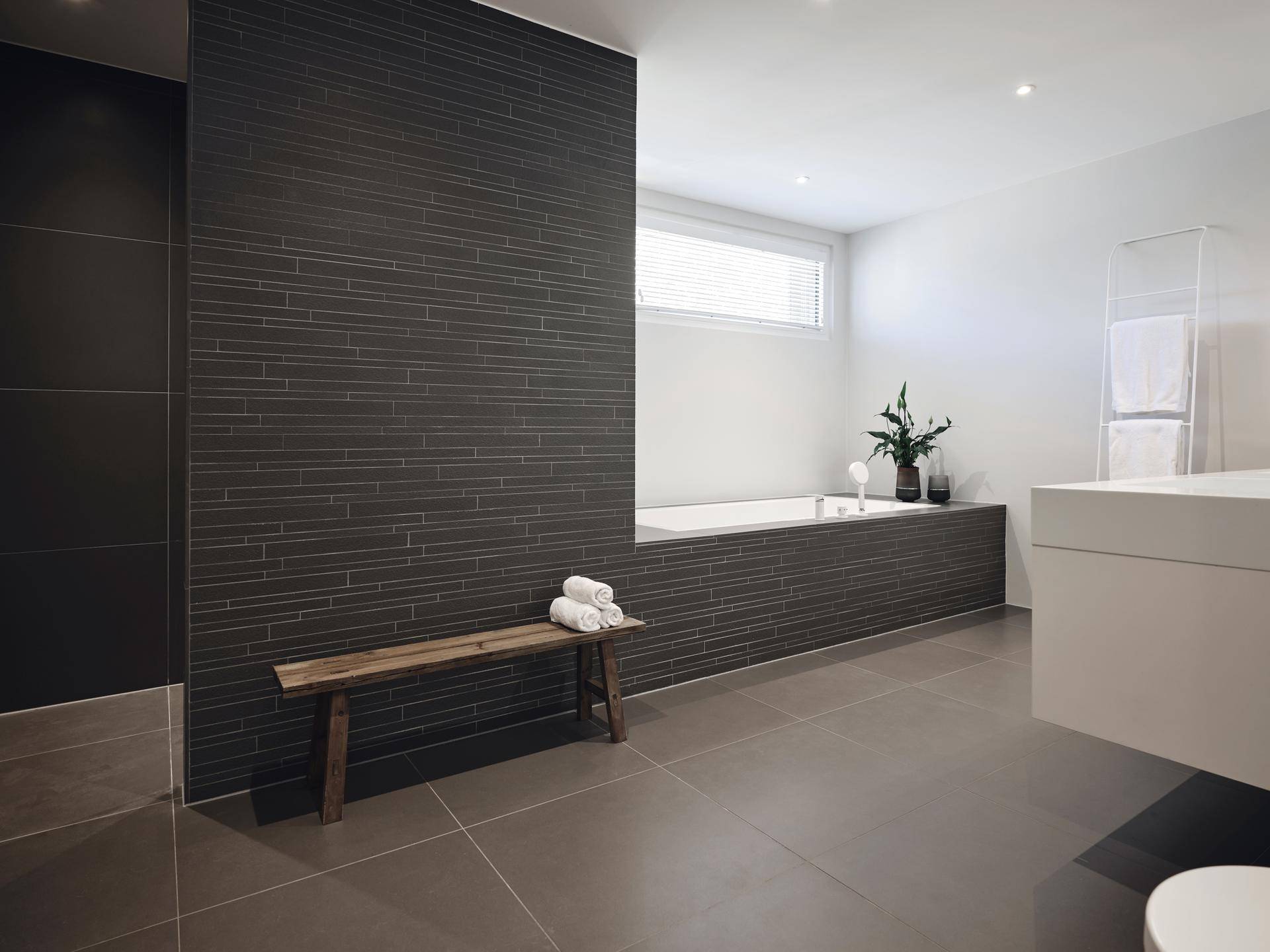 Modernes Badezimmer mit integrierter Badewanne, dunklen Fliesen und einem schwebenden Waschtisch.