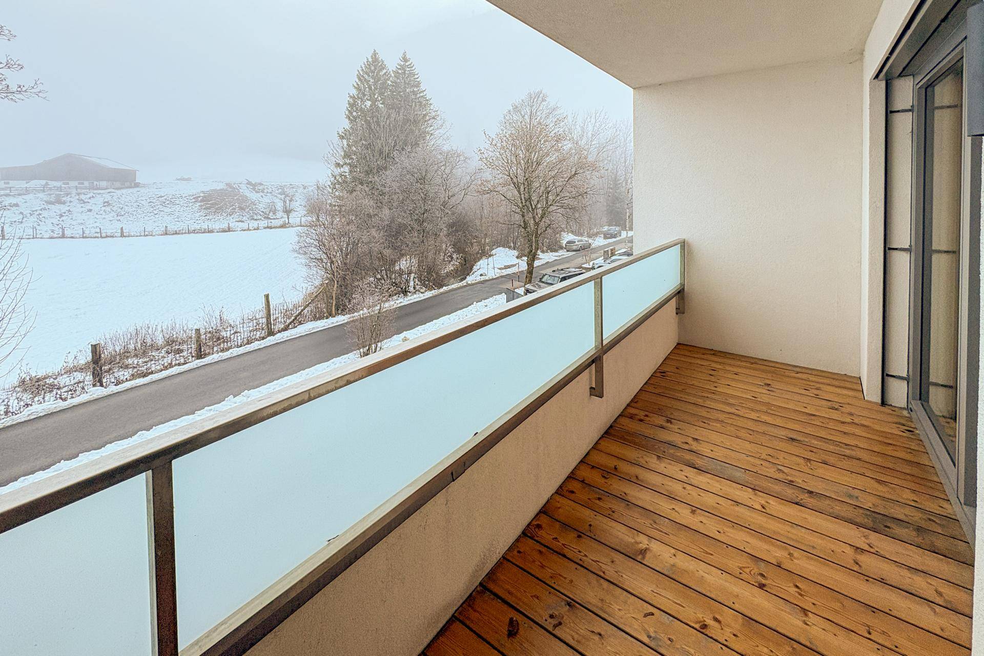 Balkon mit Holzboden und Glasbrüstung, bietet einen weiten Blick über eine verschneite Landschaft.