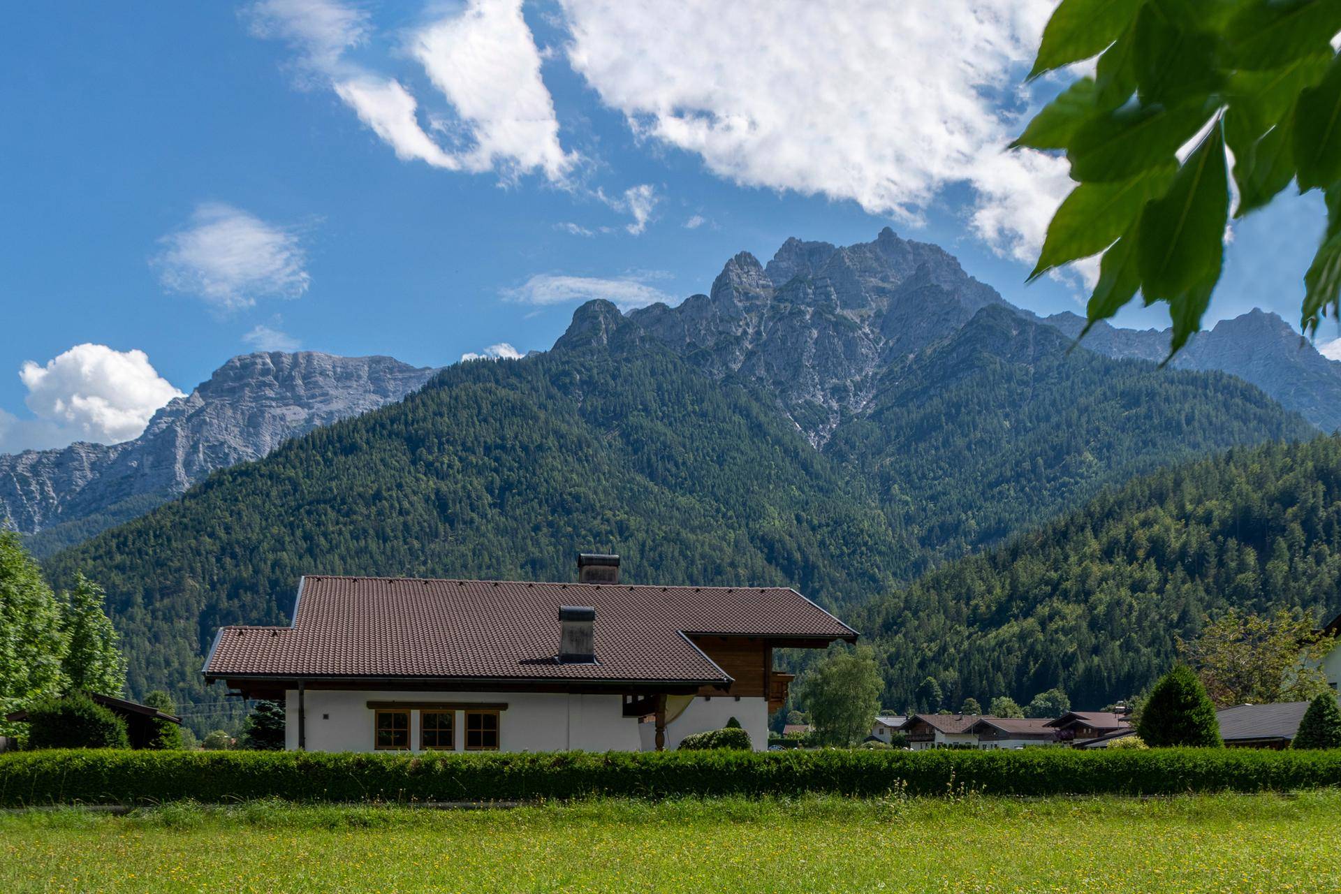Charmantes Haus mit braunem Ziegeldach und malerischem Bergblick vor bewaldeten Hängen.