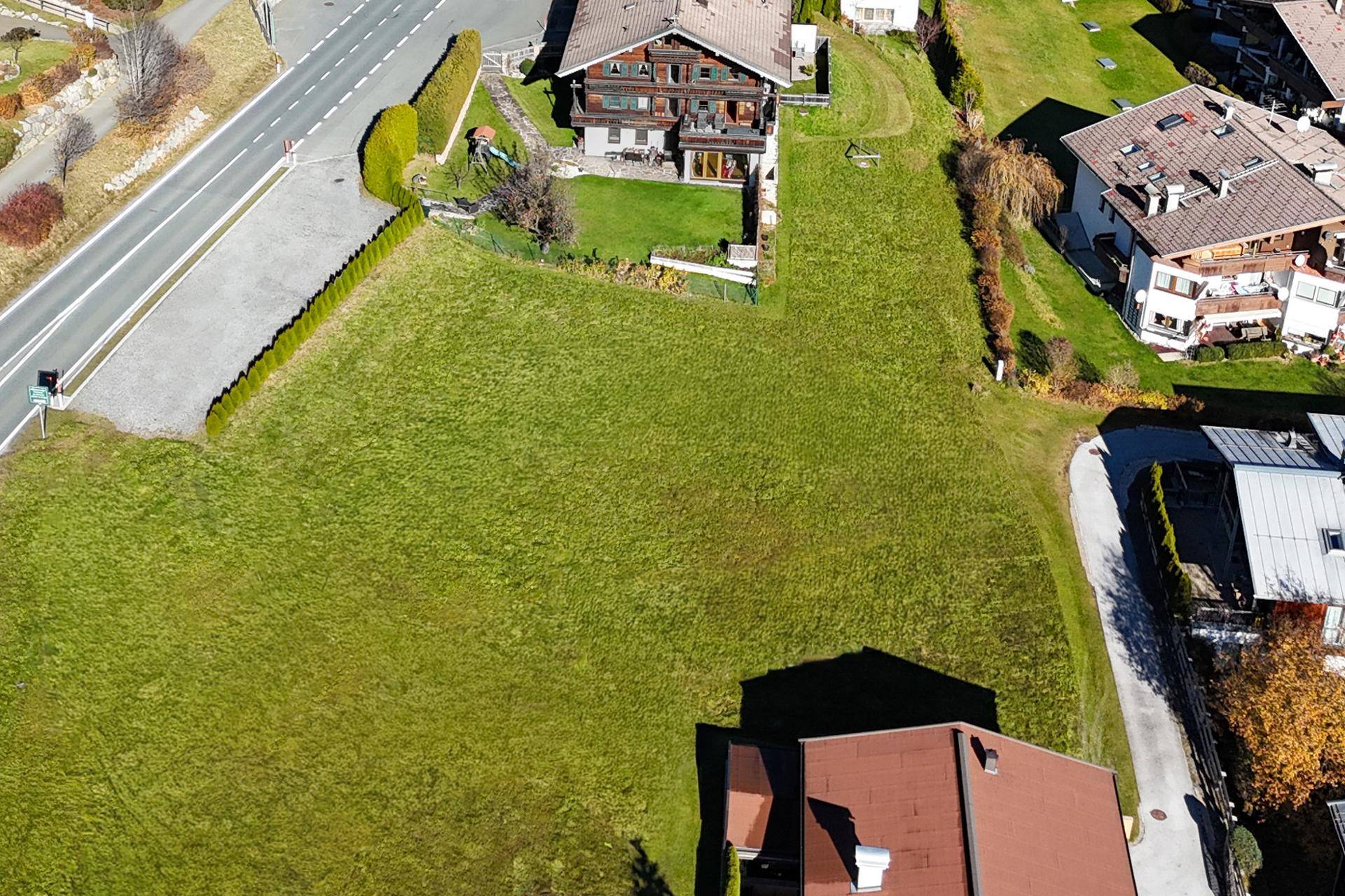 Luftaufnahme eines großen, grünen Grundstücks mit angrenzender Straße und umliegenden Wohnhäusern in sonniger Lage.