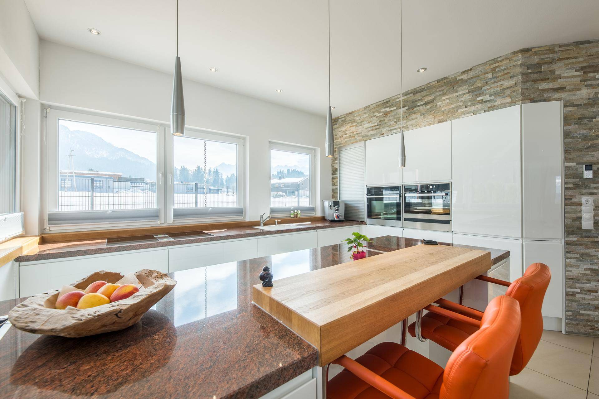 Moderne Küche mit weißen Hochglanzfronten, Granitarbeitsplatte und Bergblick durch die Fenster.