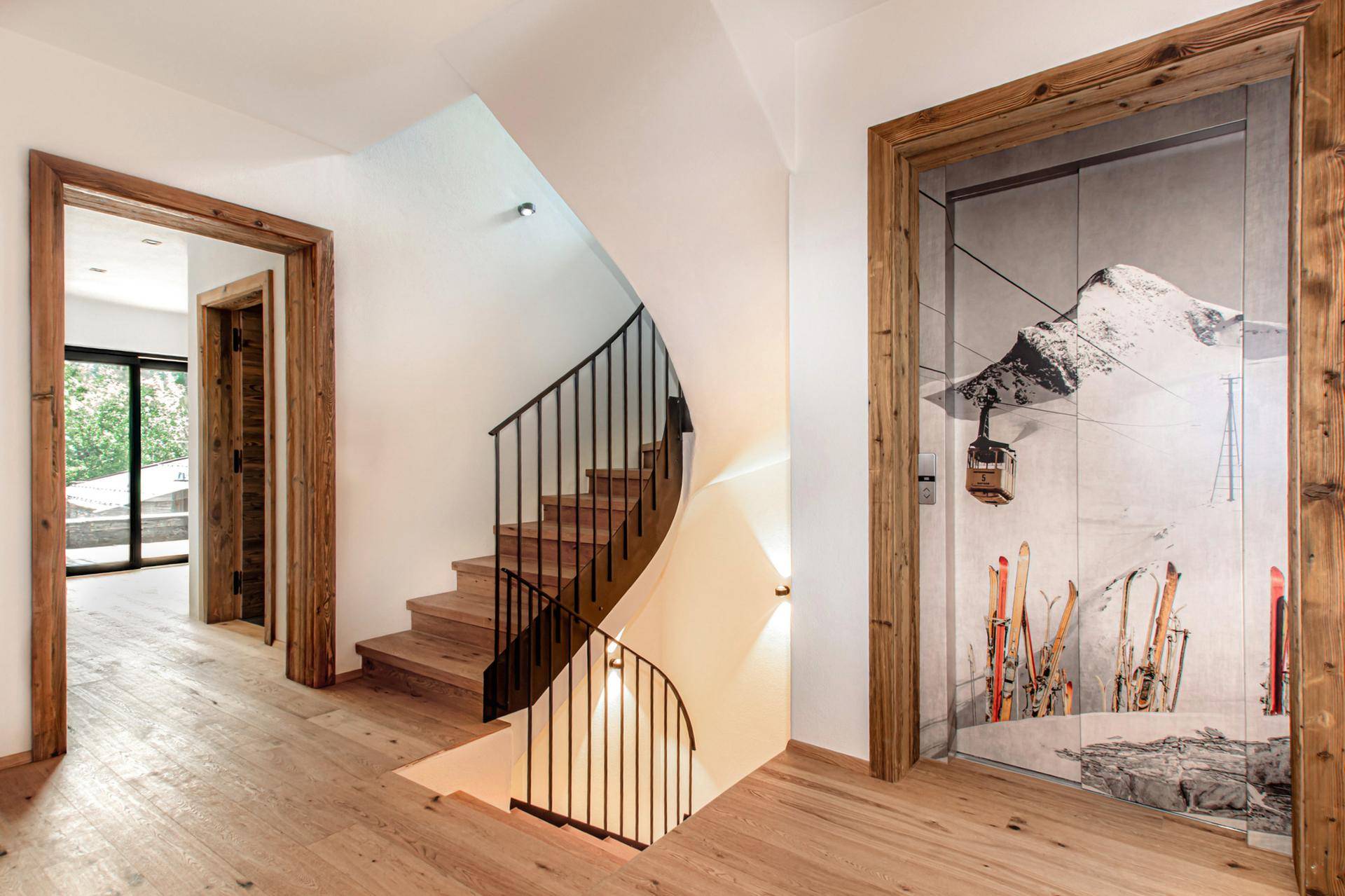 Heller Flur mit Holzfußboden, geschwungener Treppe und einem Wandbild mit Bergmotiv.