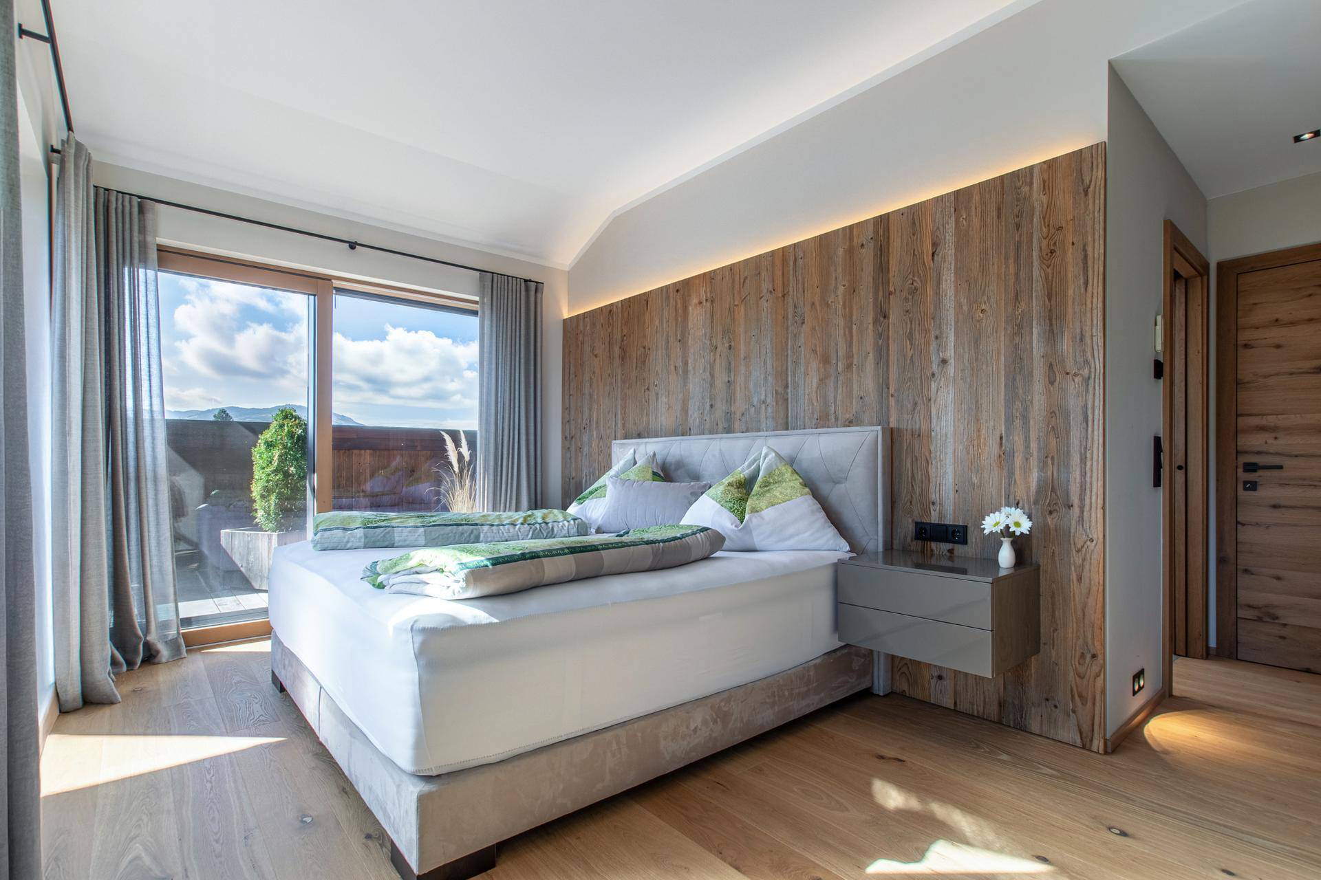 Gemütliches Schlafzimmer mit Holzwand, indirekter Beleuchtung und Balkonzugang mit Bergblick.