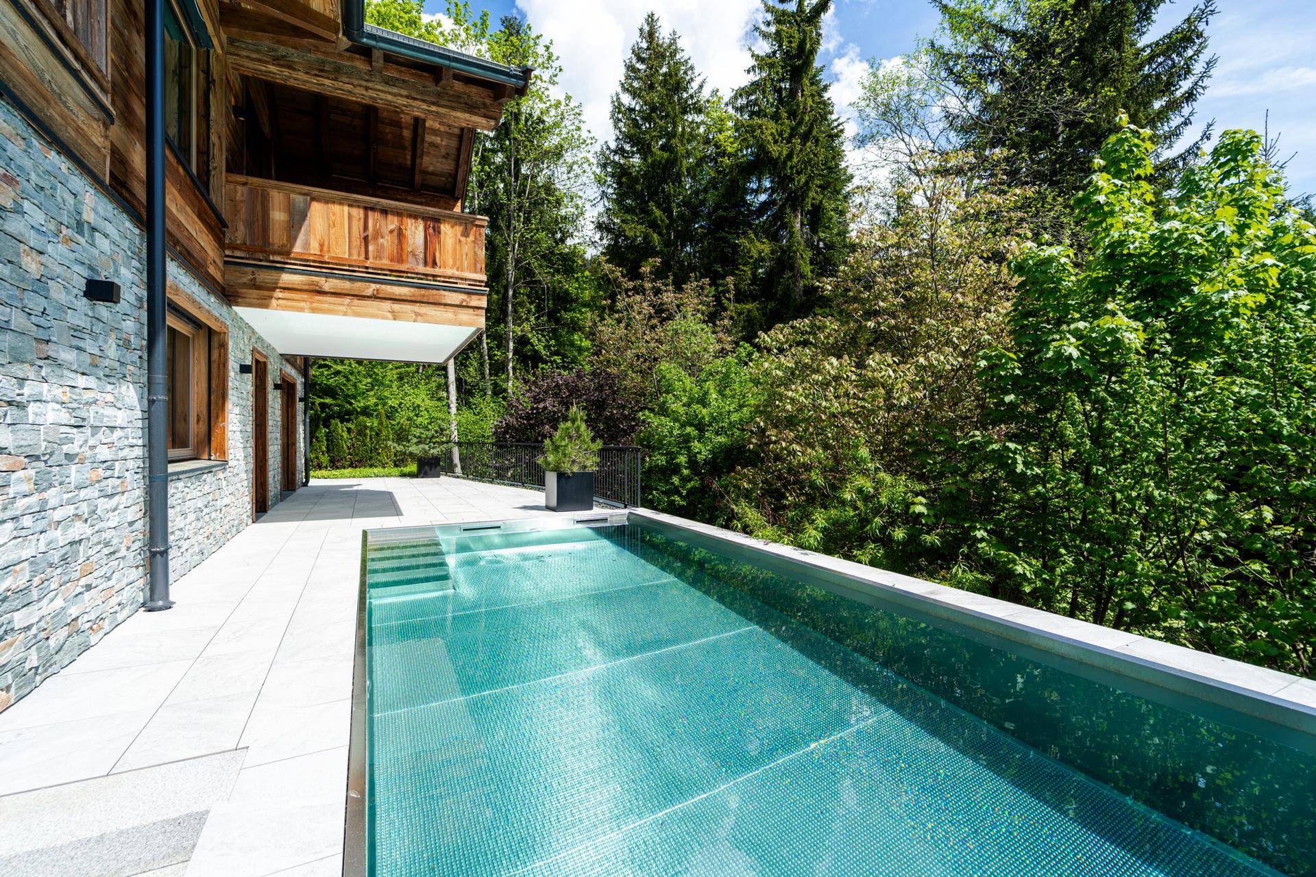 Eleganter Infinity-Pool mit Blick ins Grüne, umgeben von einer gepflegten Terrasse und Bäumen.