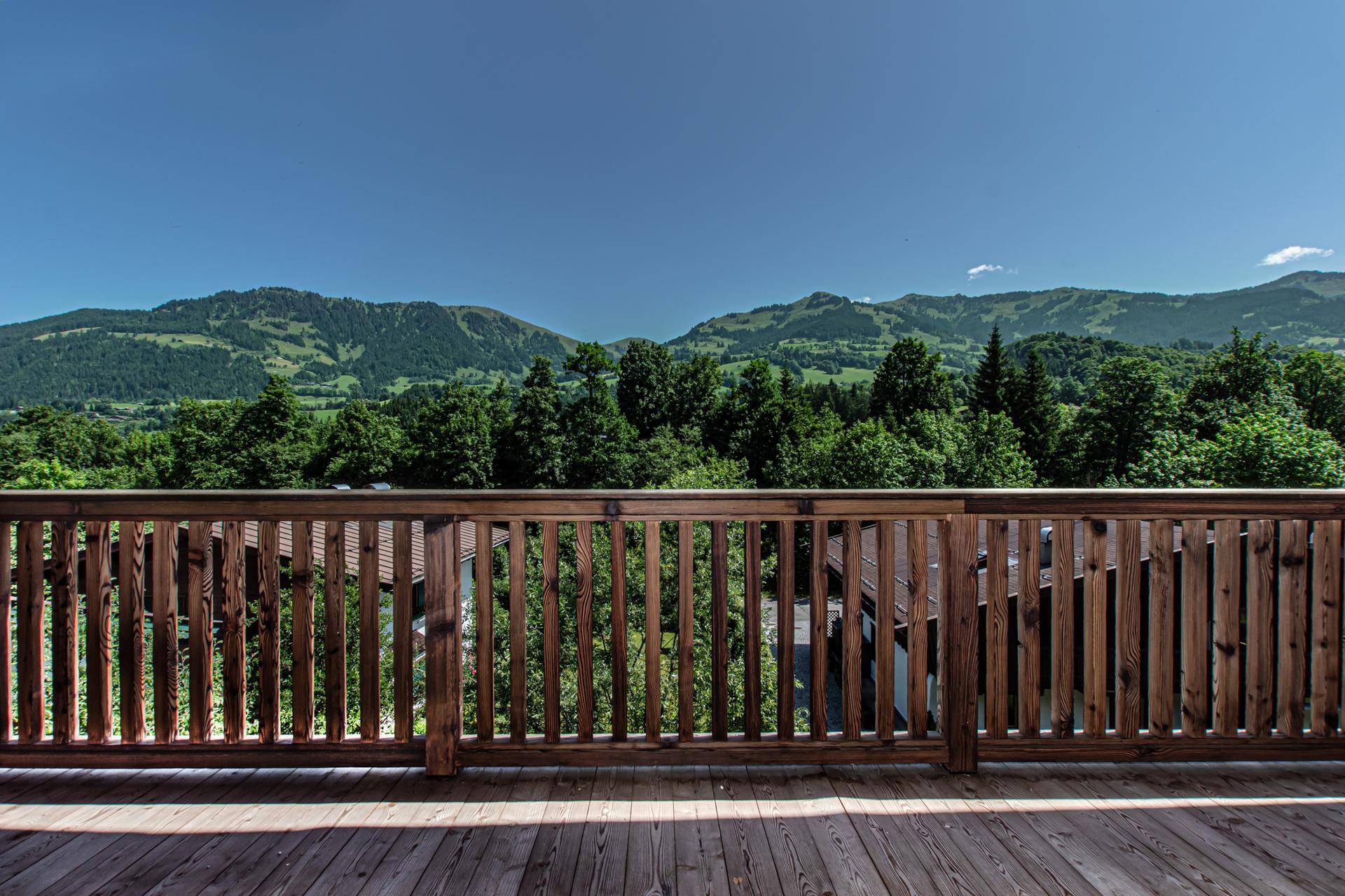 Breiter Holzbalkon mit stabiler Brüstung und weitem Blick über die grünen Berge.