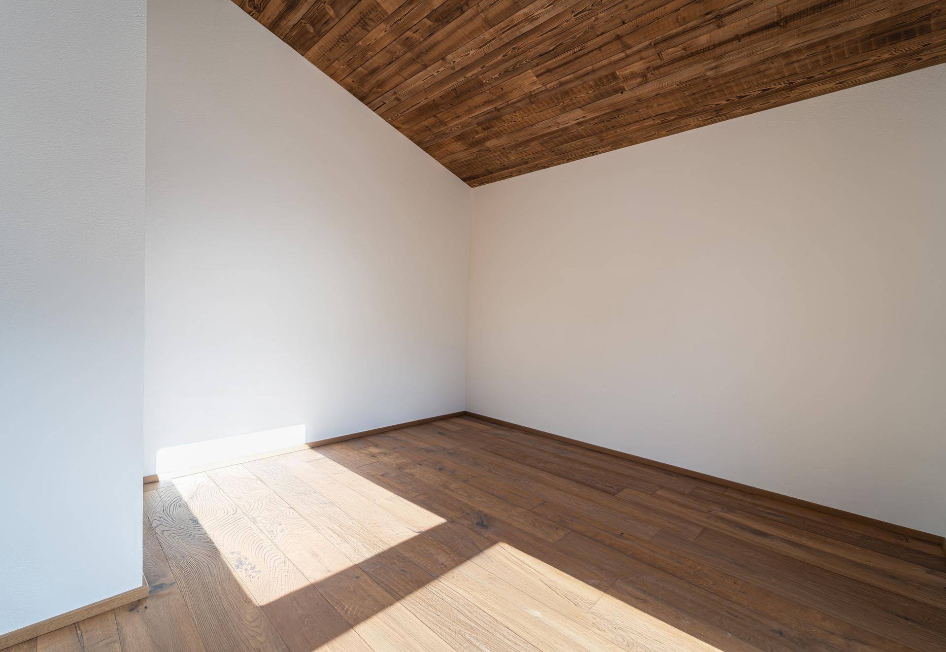 Geräumiges Zimmer mit Holzdielenboden, weißen Wänden und einer markanten Holzdecke.