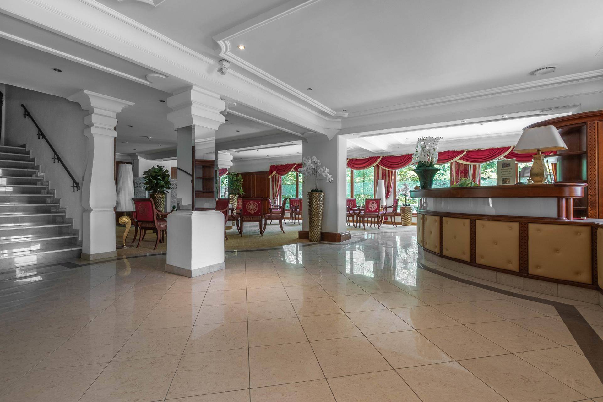 Geräumige Hotellobby mit hellem Fliesenboden, klassischer Einrichtung und einer Rezeption.