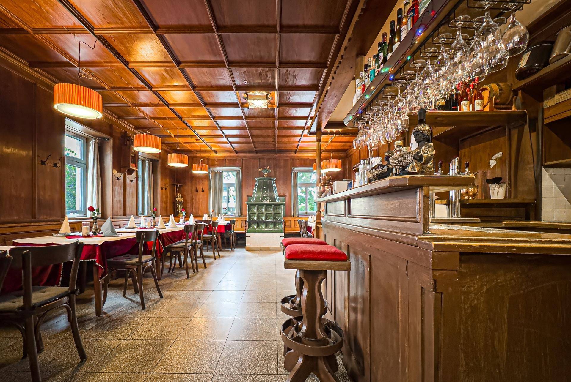 Gemütlicher Barbereich und Speisesaal mit dunkler Holztäfelung, Barhockern und einem Kachelofen.
