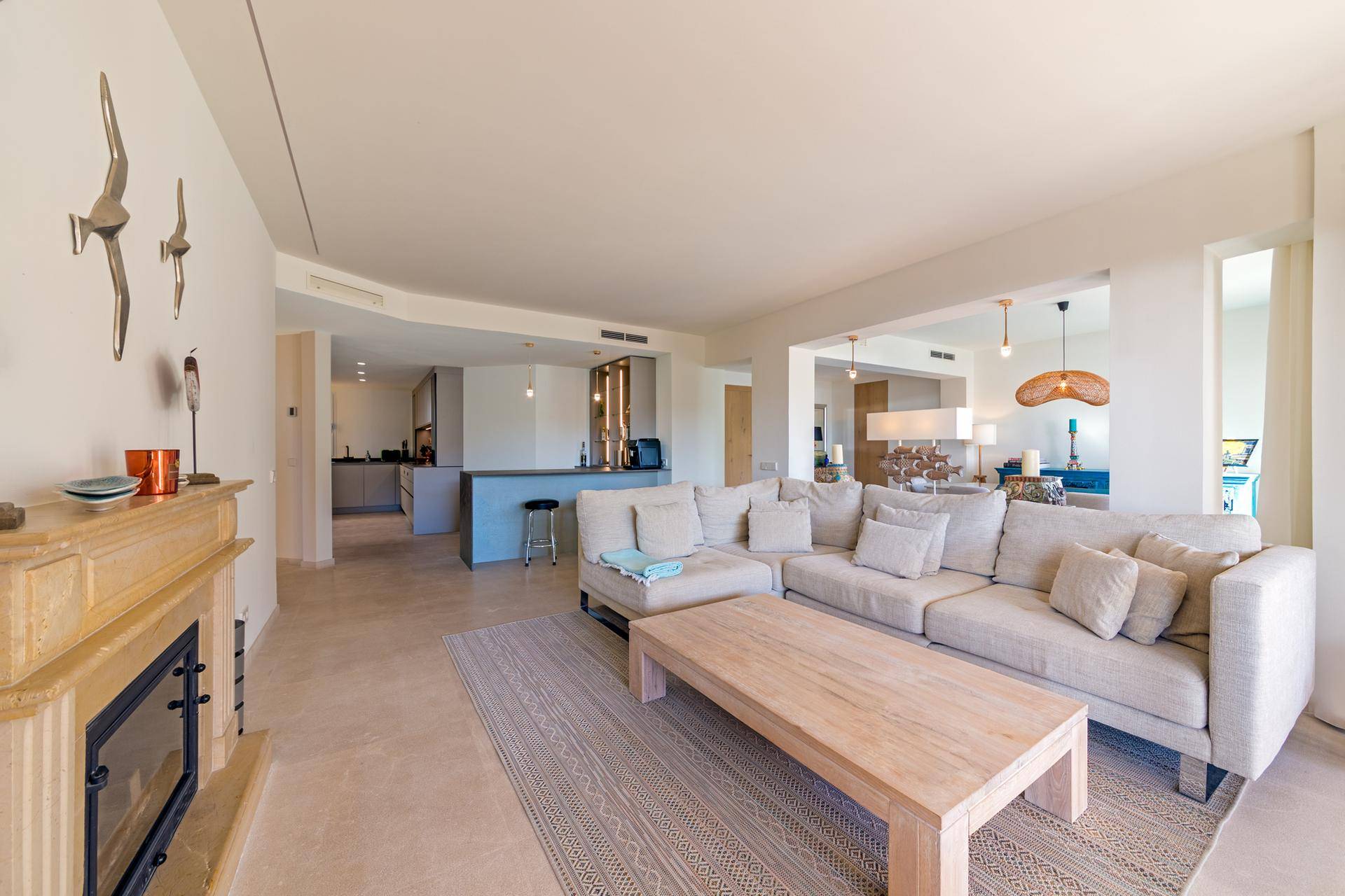 Offener Wohnbereich mit großem Sofa, Kamin und Blick auf die moderne Küche im Hintergrund.