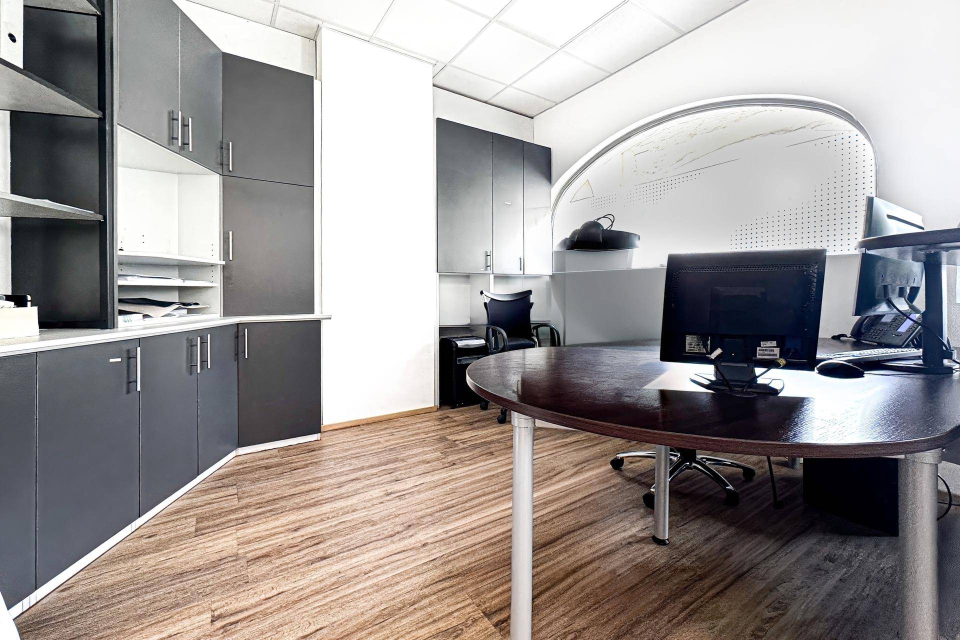 Büroecke mit dunklen Einbauschränken, Schreibtisch und Holzfußboden.
