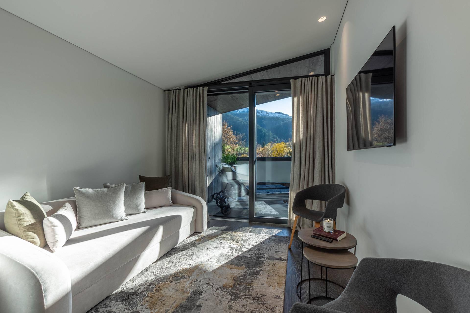 Gemütliches Wohnzimmer mit bequemer Couch, Wandfernseher und Zugang zu einem Balkon mit Bergblick.