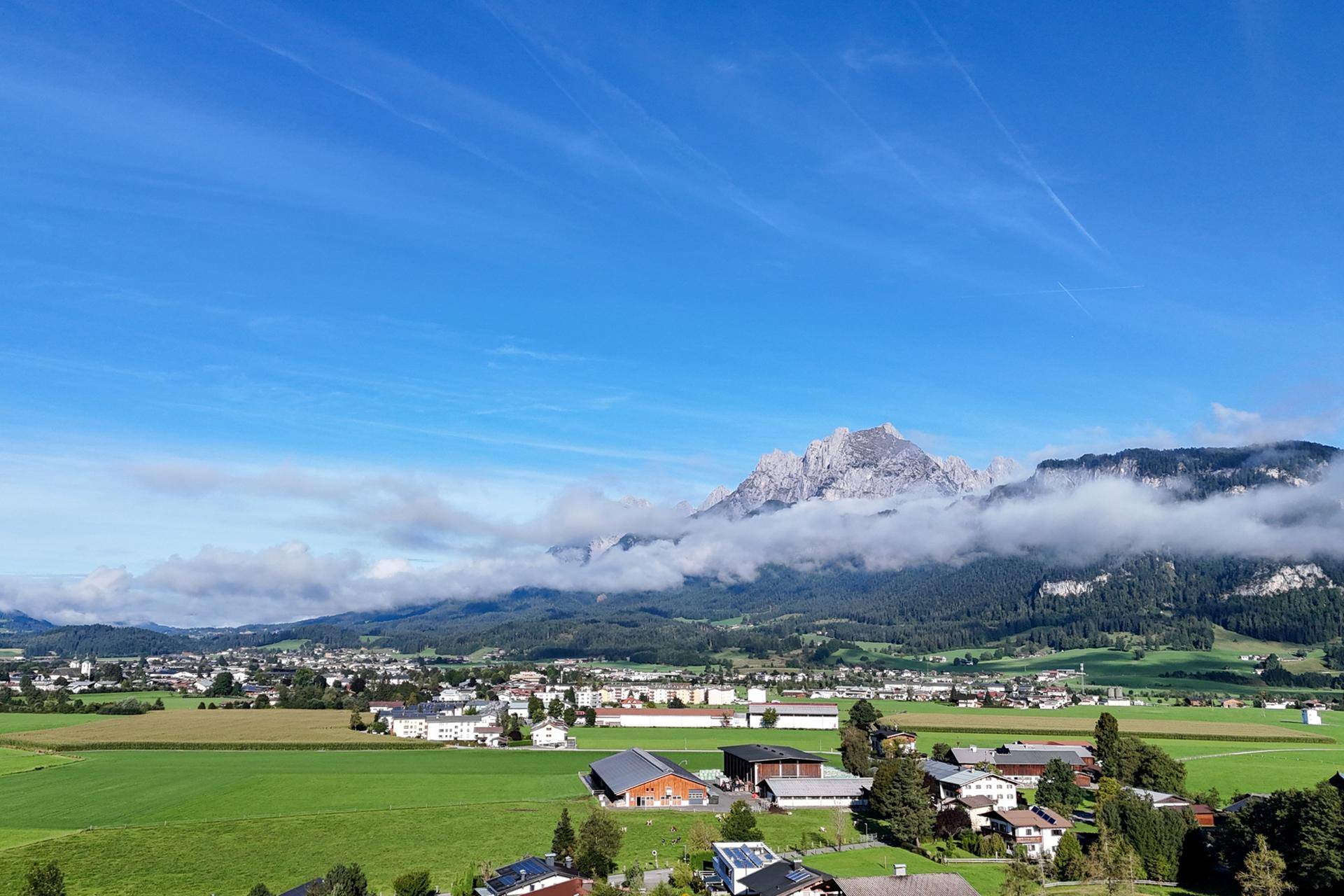 Panoramablick auf eine malerische Stadt im Tal, umgeben von grünen Feldern und majestätischen Bergen.