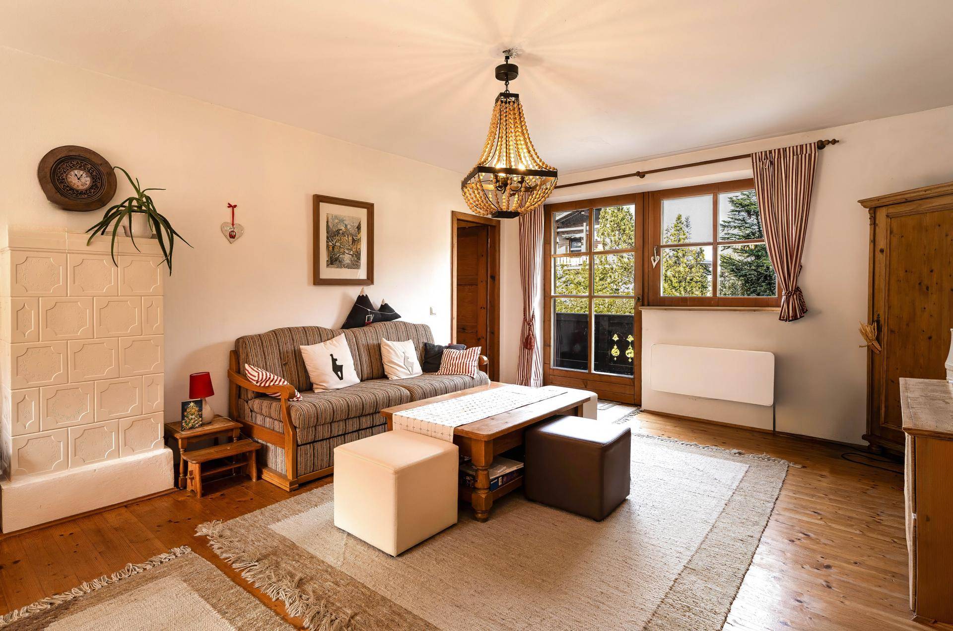 Helles Wohnzimmer mit Kachelofen, Holzboden und Zugang zum Balkon mit Bergblick.